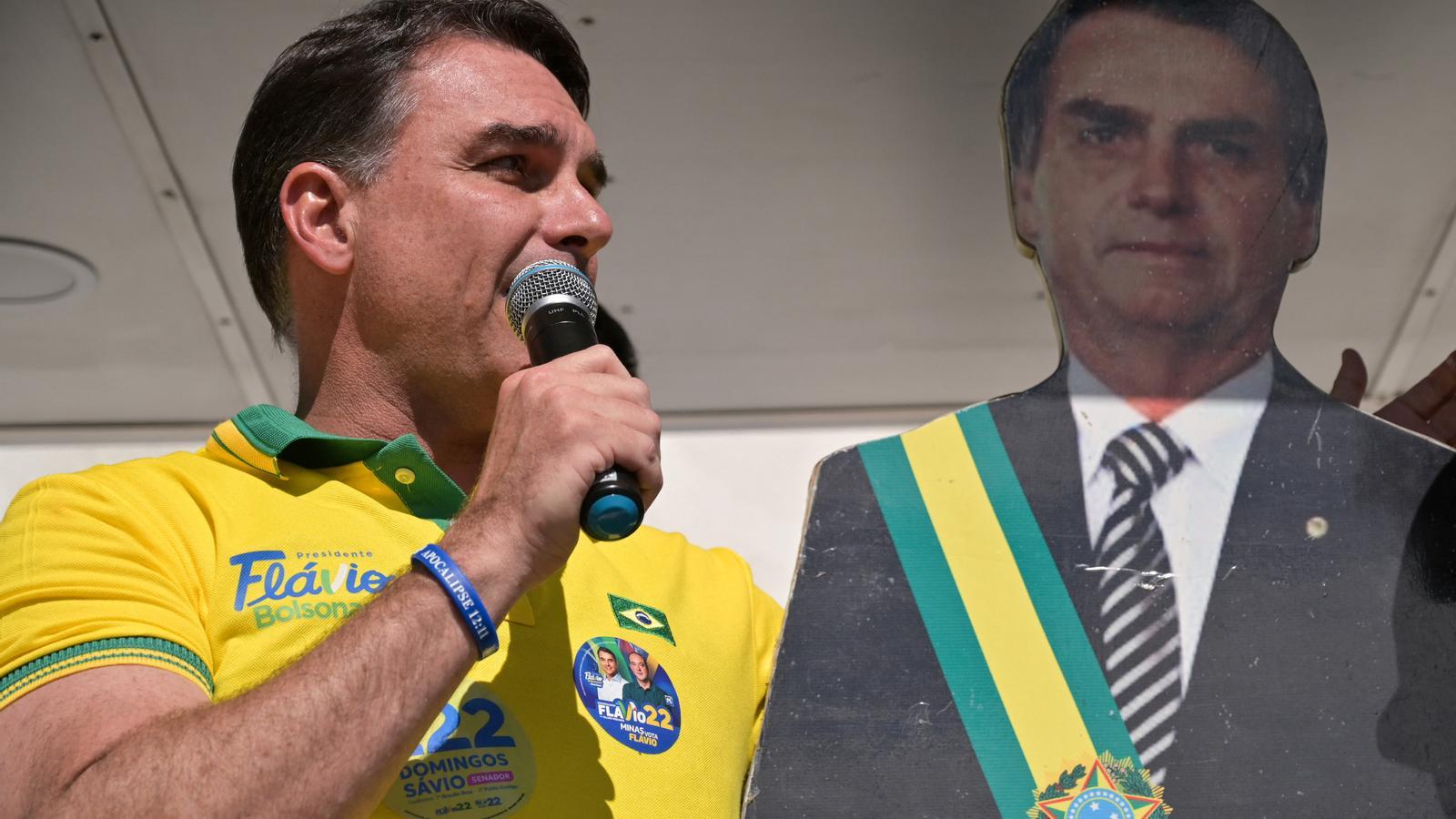 The Brazilian far-right candidate, Flávio Bolsonaro, holding an image of his father and former president, Jair Bolsonaro, at a campaign rally.
