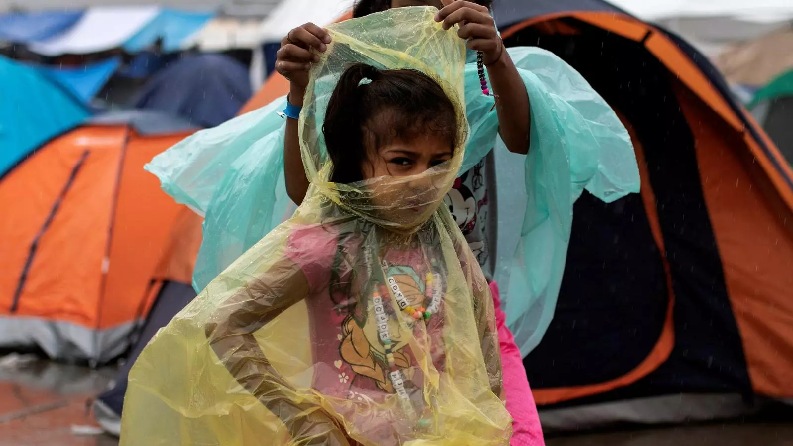 Dues nenes centreamericanes intenten protegir-se de la pluja en un campament per a refugiats a Tijuana