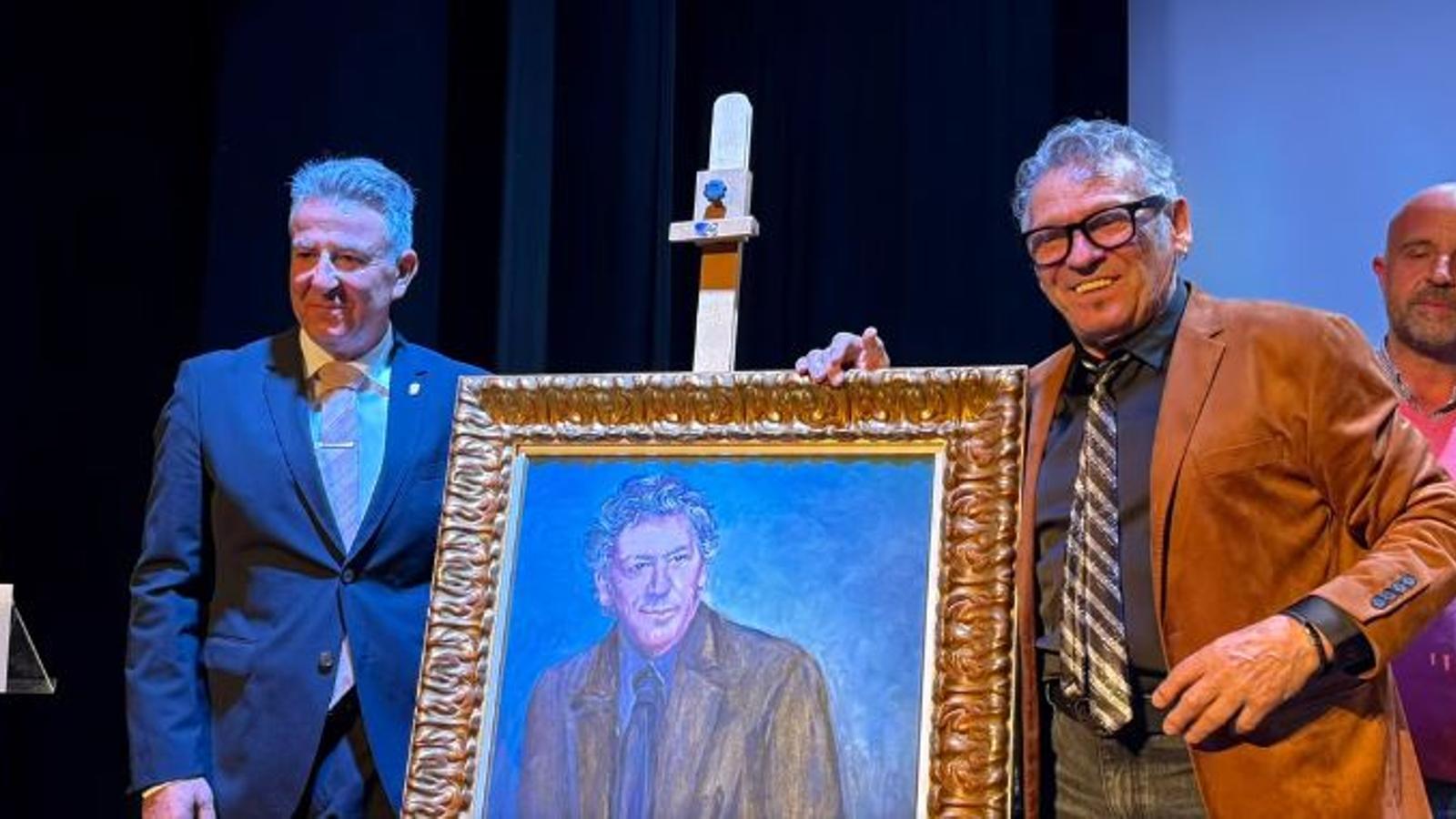 El cantant Llorenç Santamaria i el batle de Santa Maria, Nicolau Canyelles, posen amb un retrat de l'artista.