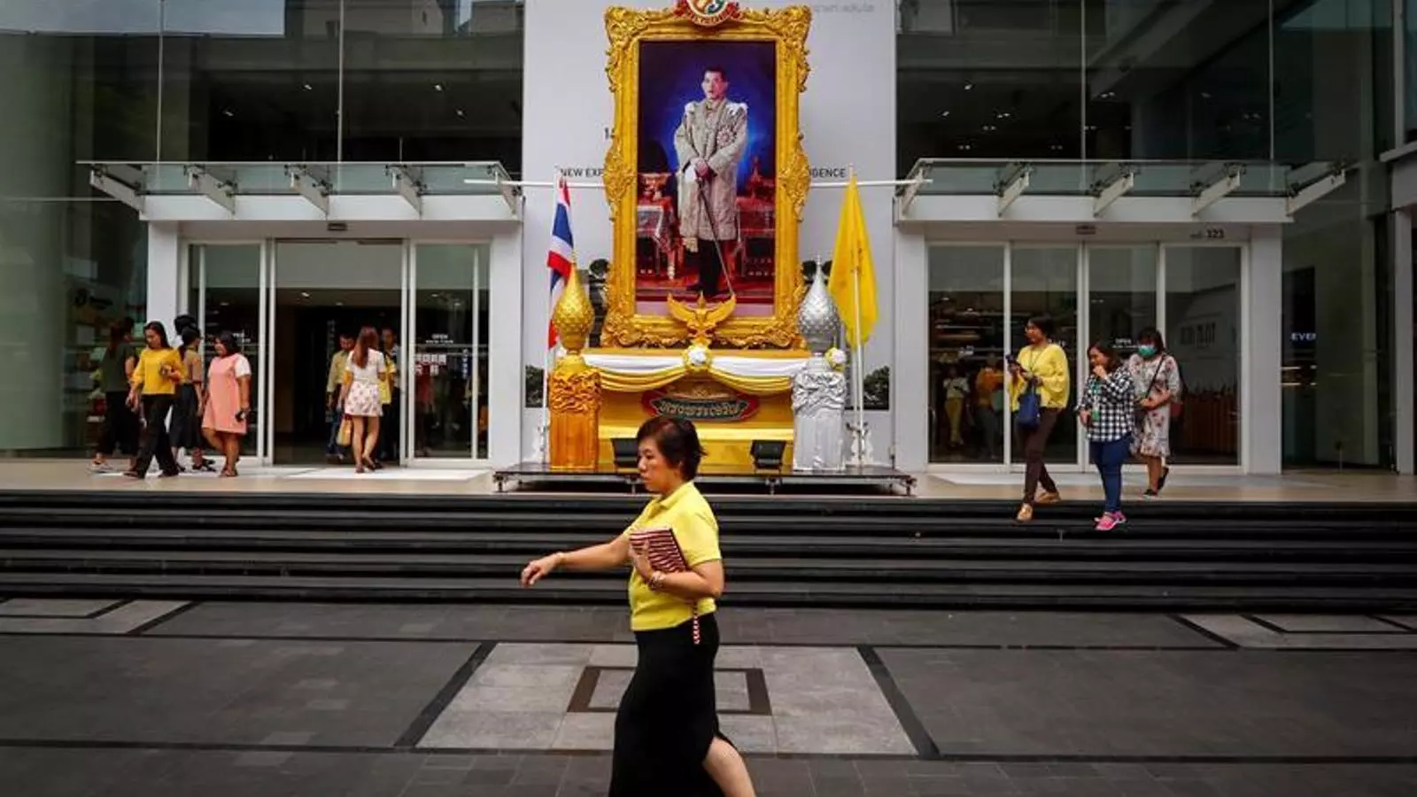 Una dona amb jersei groc passejant per davant d'un retrat del rei Maha Vajiralongkorn, en un centre comercial de Bangkok