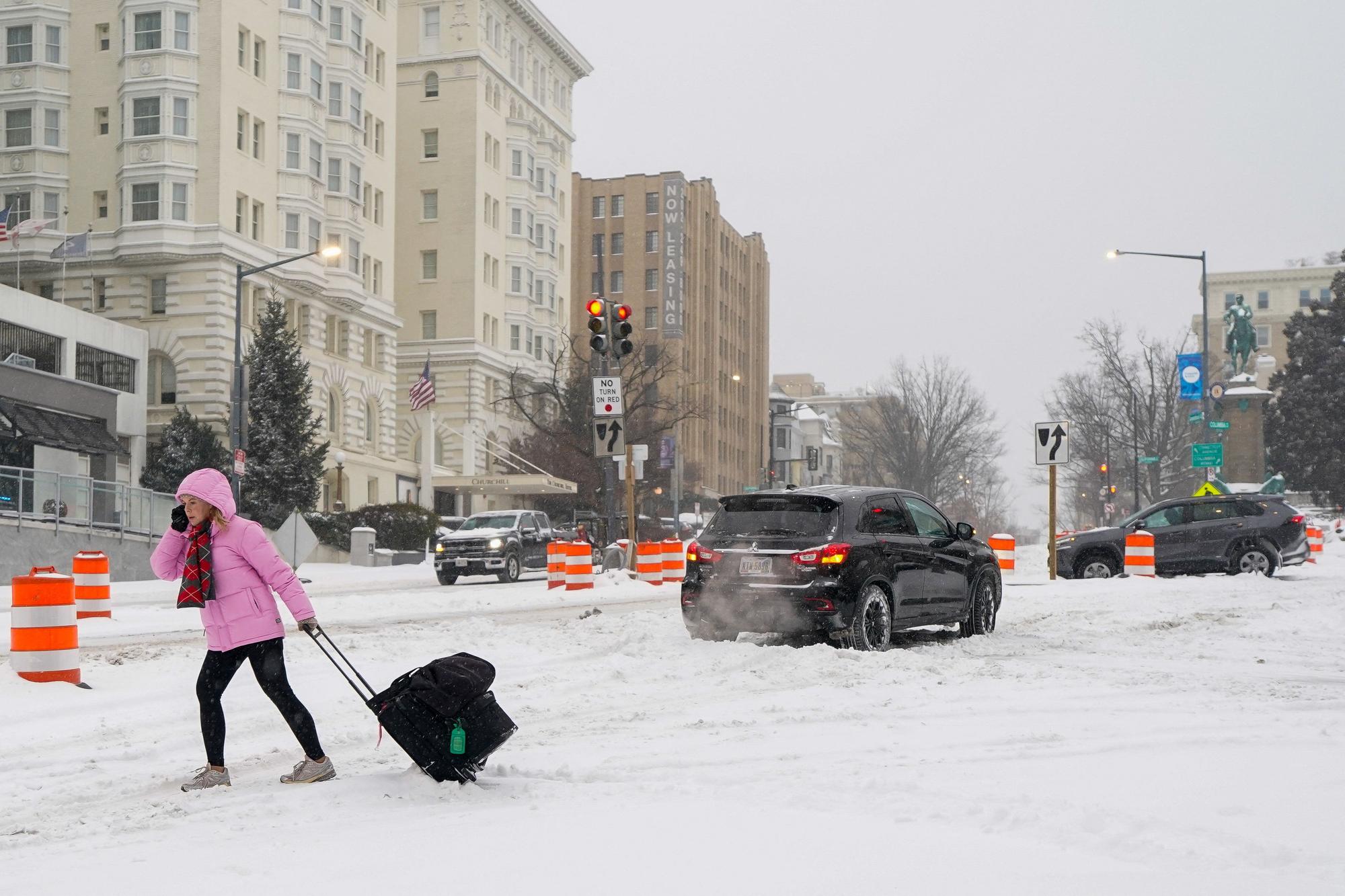 Una dona arrossega una maleta en una avinguda de Washington coberta de neu.