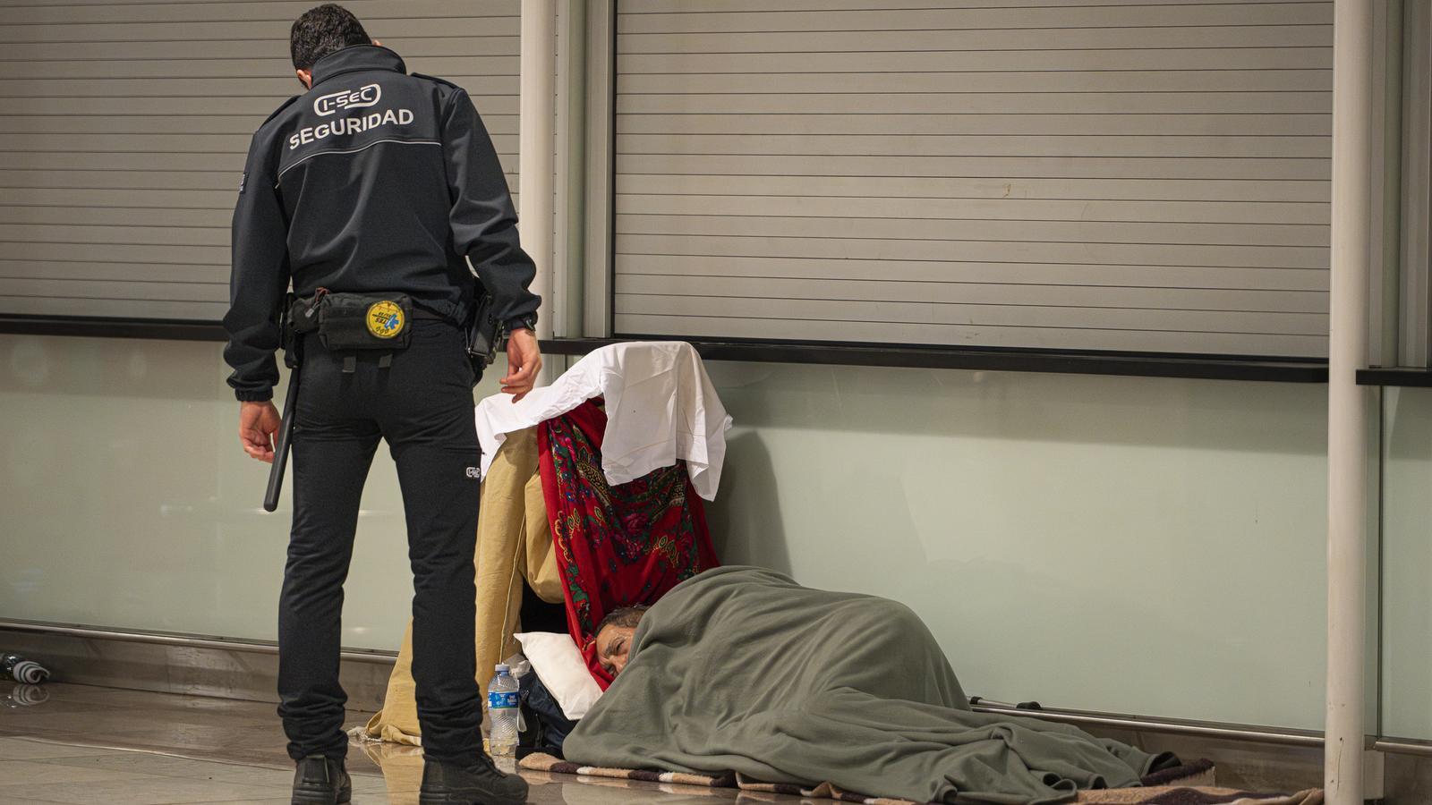 A security guard talks to a man spending the night at El Prat airport-