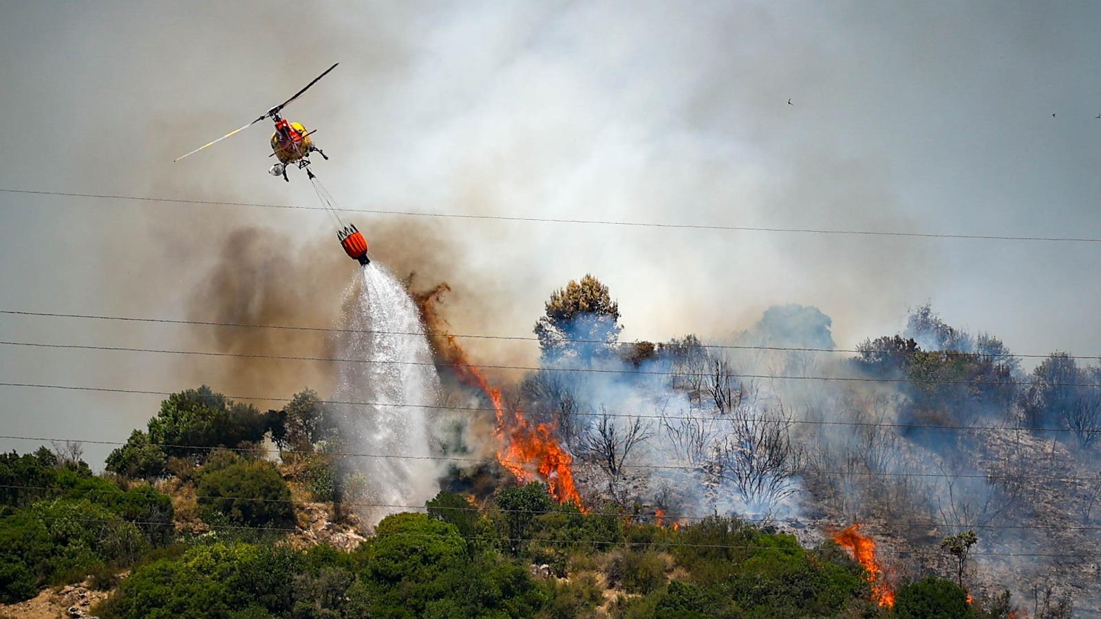 Un helicóptero de los Bomberos lanza una descarga de agua sobre las llamas del incendio declarado en Tiana.
