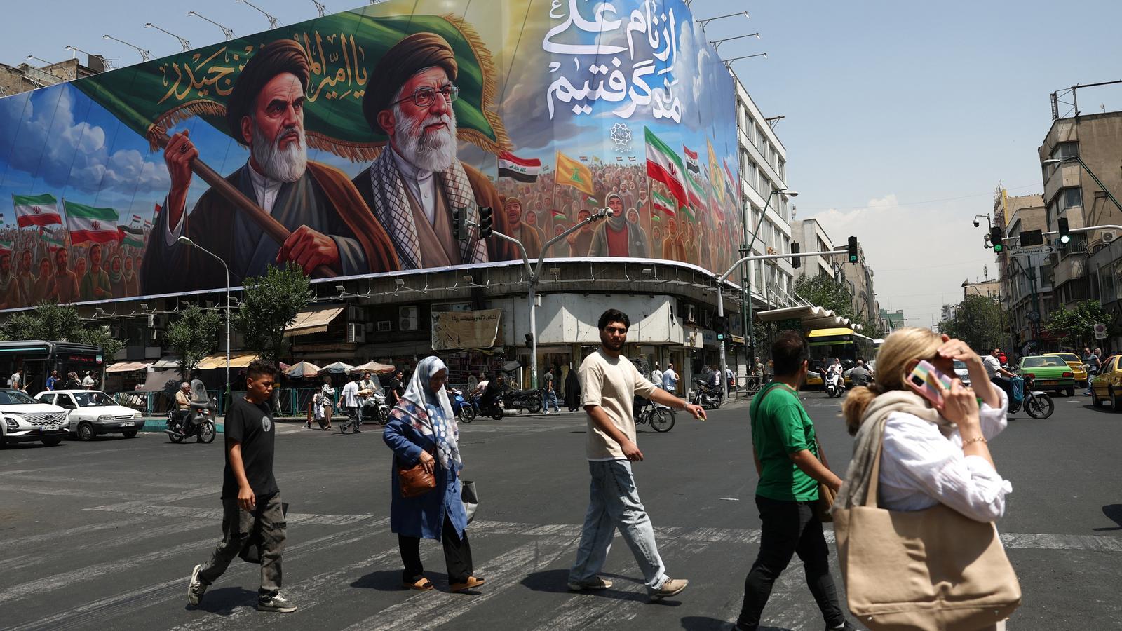 Diversas personas caminan con un mural al fondo que representa al difunto líder de la Revolución Islámica, el ayatolá Ruhollah Khomeini, y al difunto líder supremo de Irán, el ayatolá Ali Jamenei, en una calle de Teherán, Irán, el 6 de junio.