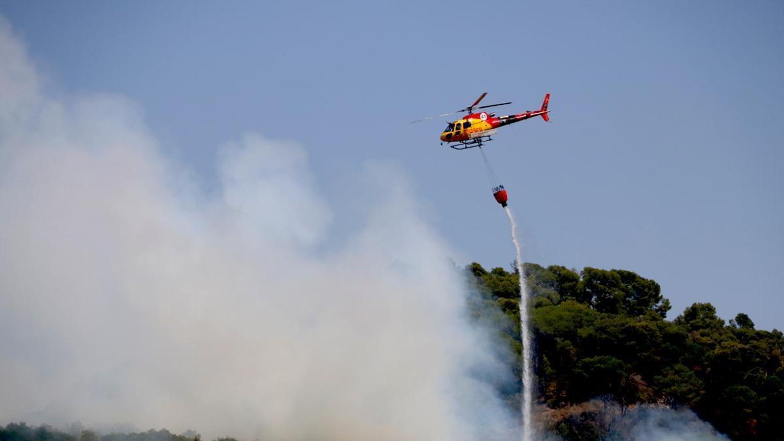 A helicopter drops water on a forest fire in Alforja.