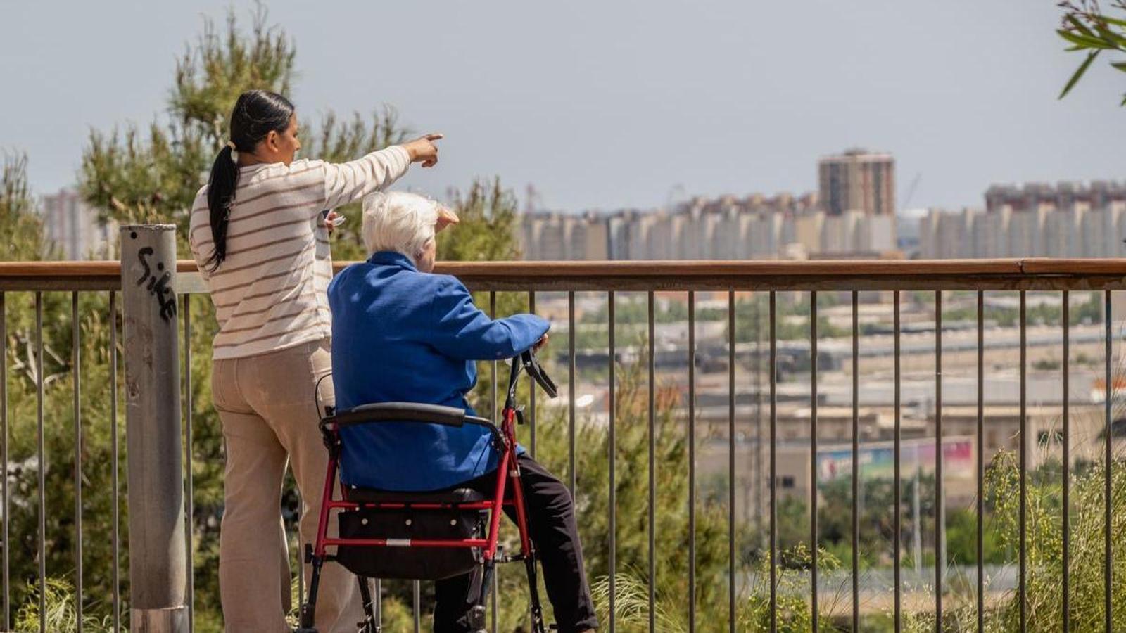 A woman sitting on a walker and her caregiver, in Cornellà.