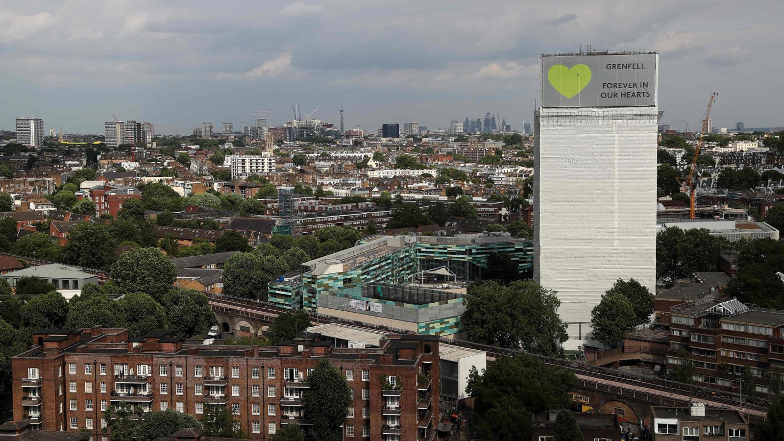 Una imagen de la Torre Grenfell, envuelta con una lona y con el eslogan en lo alto de todo “Grenfell, siempre en nuestros corazones”.