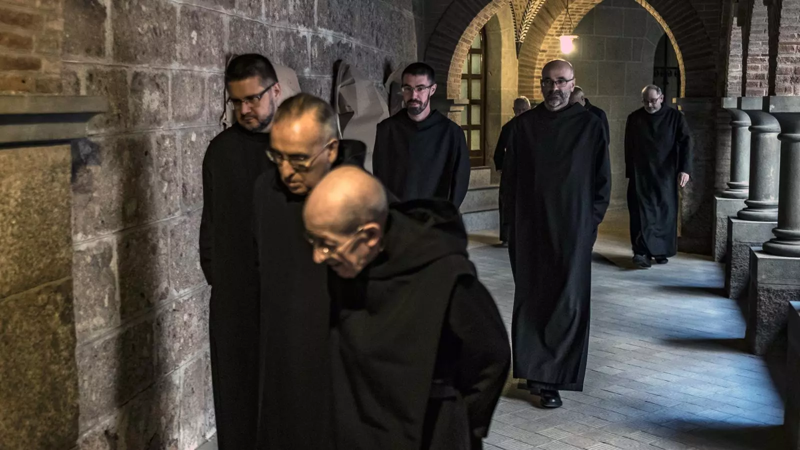 Un grup de monjos caminen pel claustre romànic refet als anys 20 del segle XX per Josep Puig i Cadafalch, sortint del refetori després de dinar en silenci.