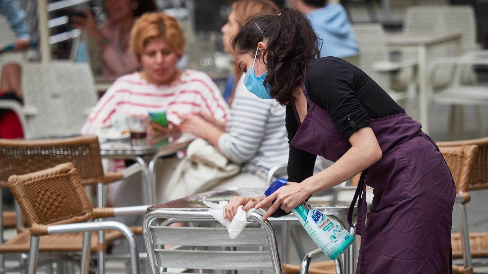 Una dona desinfectant un taula del restaurant.