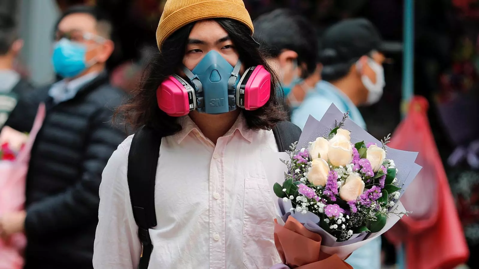 Un jove camina pels carrers de Hong Kong amb una mascara anti-gas i un ram de roses per celebrar Sant Valentí