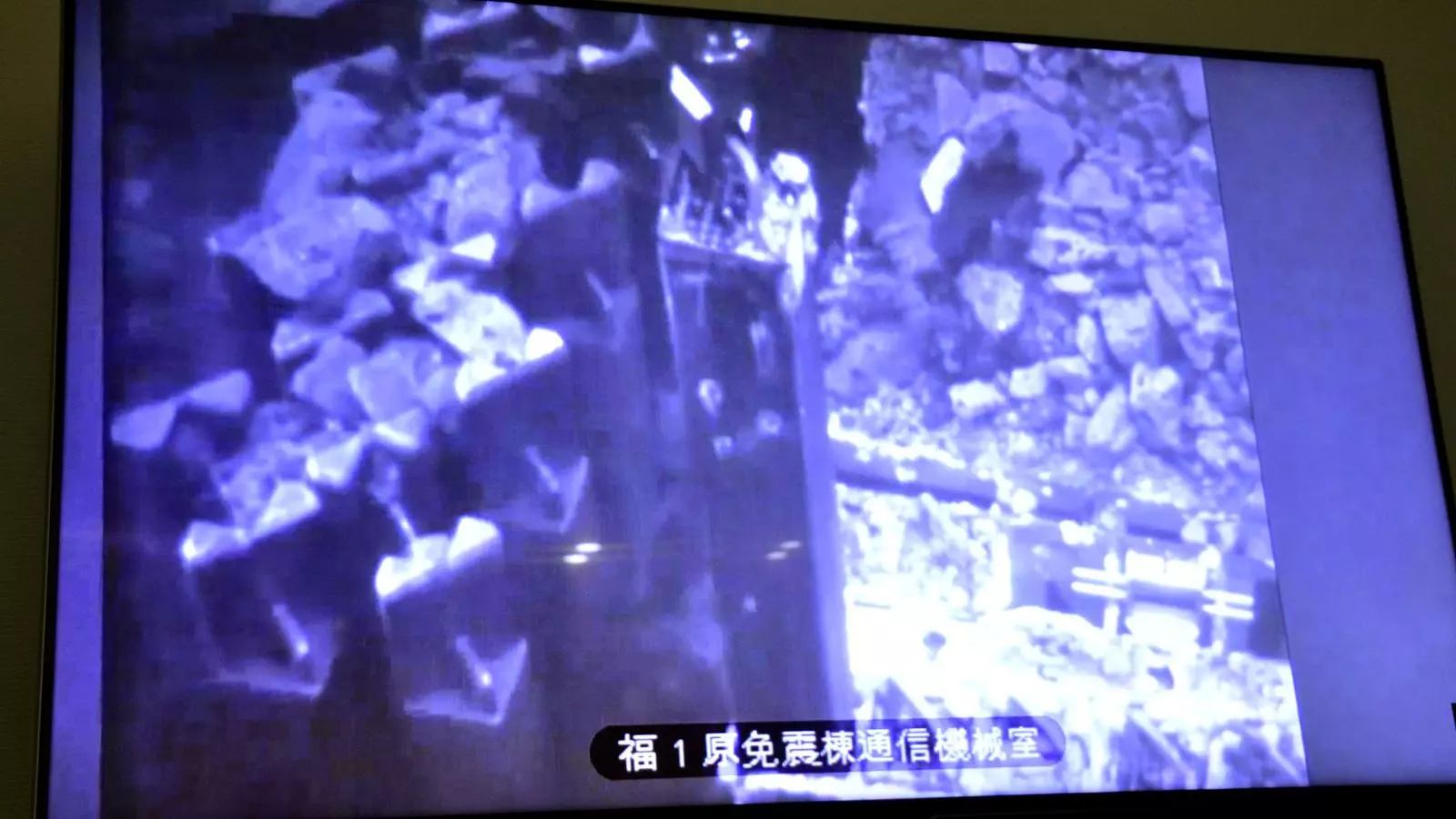 Un monitor al centre de control mostra com un robot retira les barres de combustible del reactor danyat.