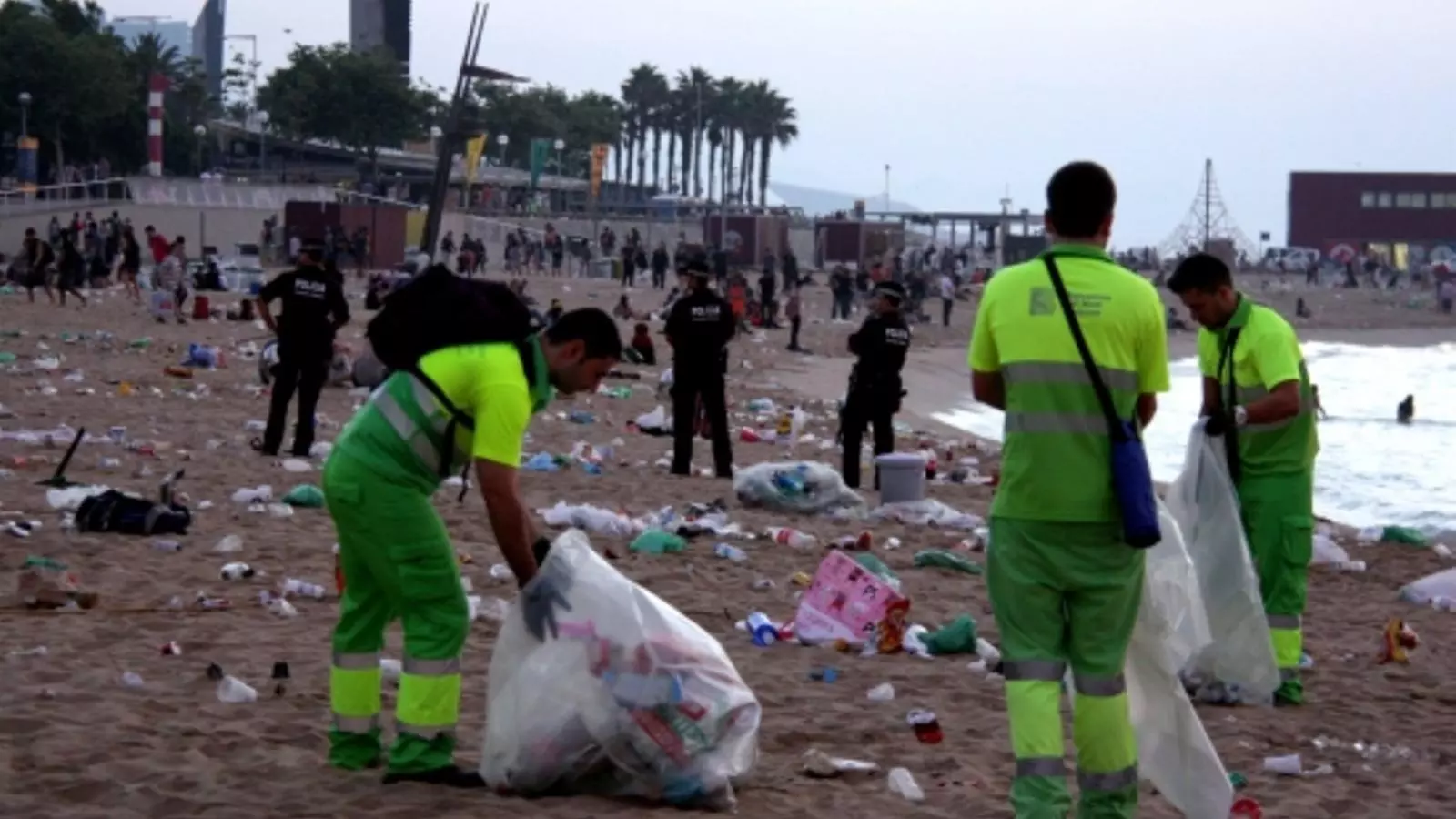 Operaris de neteja recullen les restes de la revetlla de Sant Joan a la platja de la Nova Icària de Barcelona, mentre agents de la Guàrdia Urbana desallotgen la platja / ACN