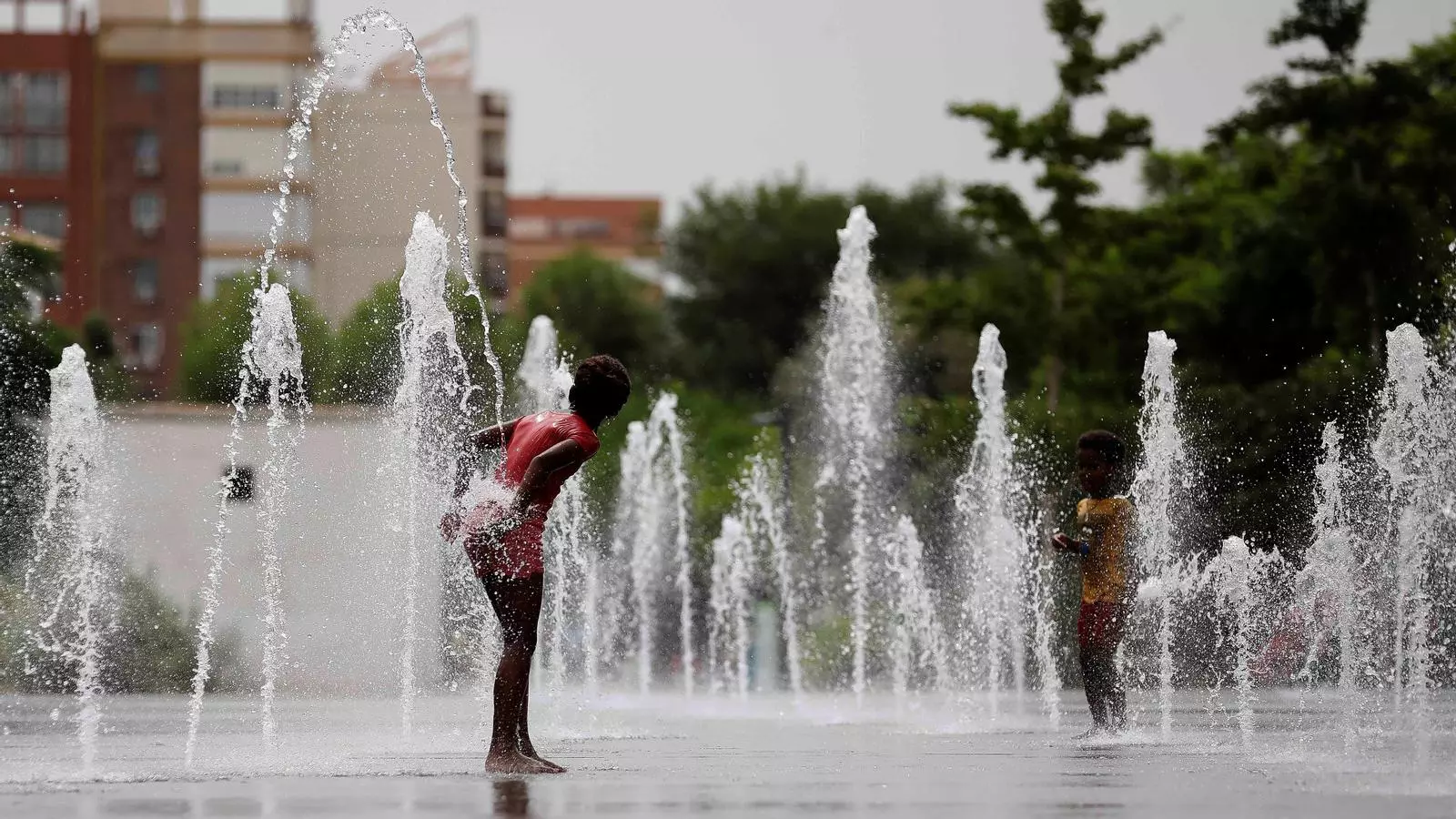 Dos nens es refresquen en una font a la ciutat de València