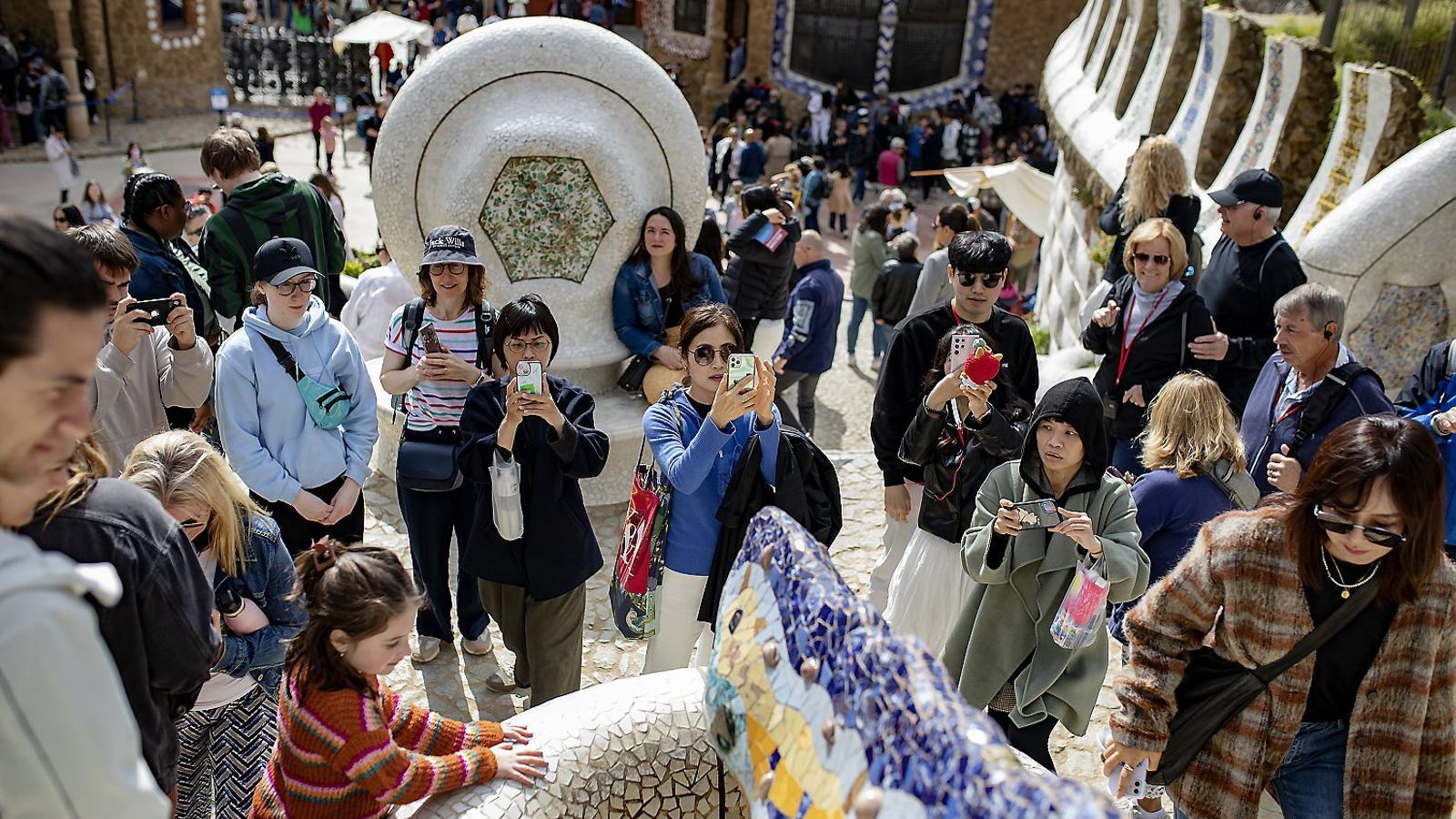 A group of tourists of different nationalities observing and taking photos of the dragon in Park Güell, in Barcelona.
