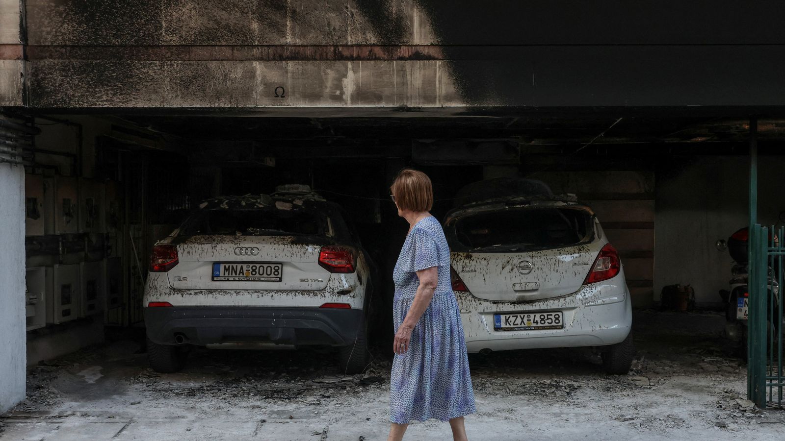 A woman walks past the building and the damaged cars after attacks on three residential buildings in Thessaloniki linked to the Greek ruling party