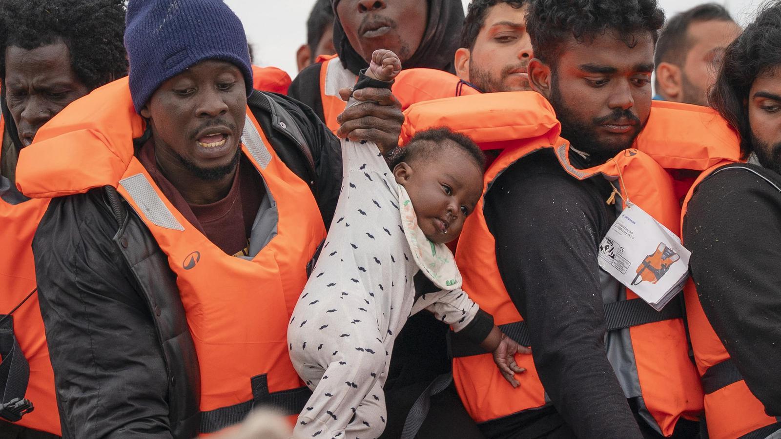 A man holds a baby dressed in pajamas as migrants board a taxi boat on the beach of Ecault, in France, before attempting to cross the English Channel.
