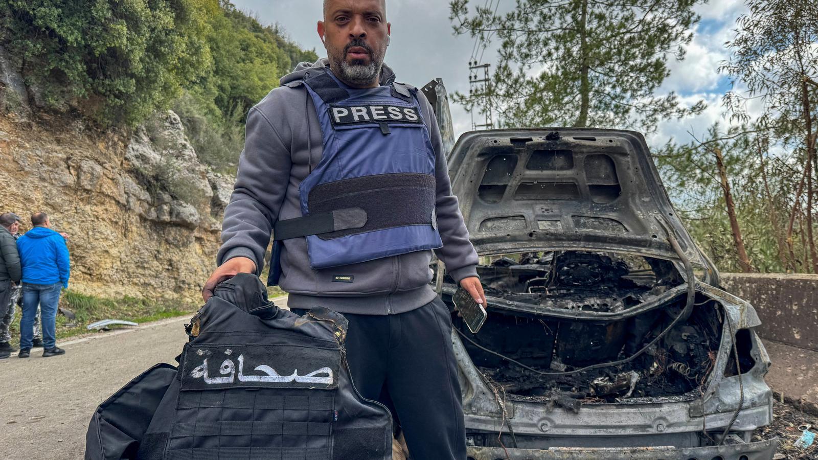 El periodista de Al Mayadeen, Jamal Al-Gharabi, sostiene un chaleco de prensa al lado de un coche destruido por un ataque israelí dirigido que ha matado a periodistas libaneses.