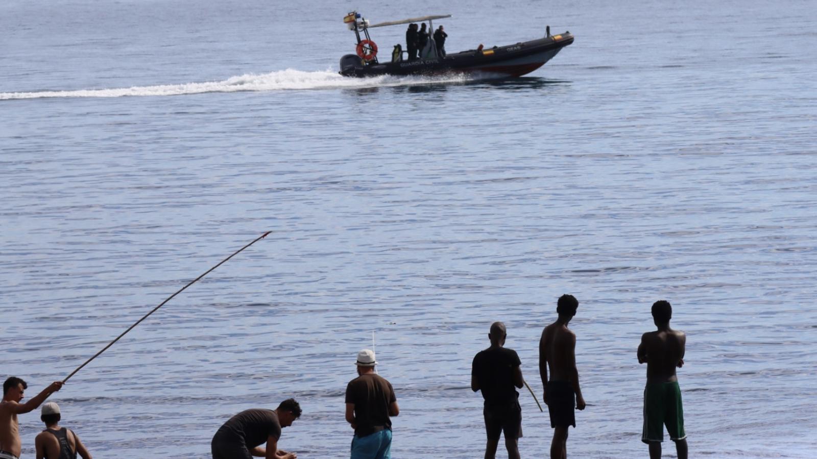 A Guardia Civil boat in front of a group of migrants living in squalor in Ceuta