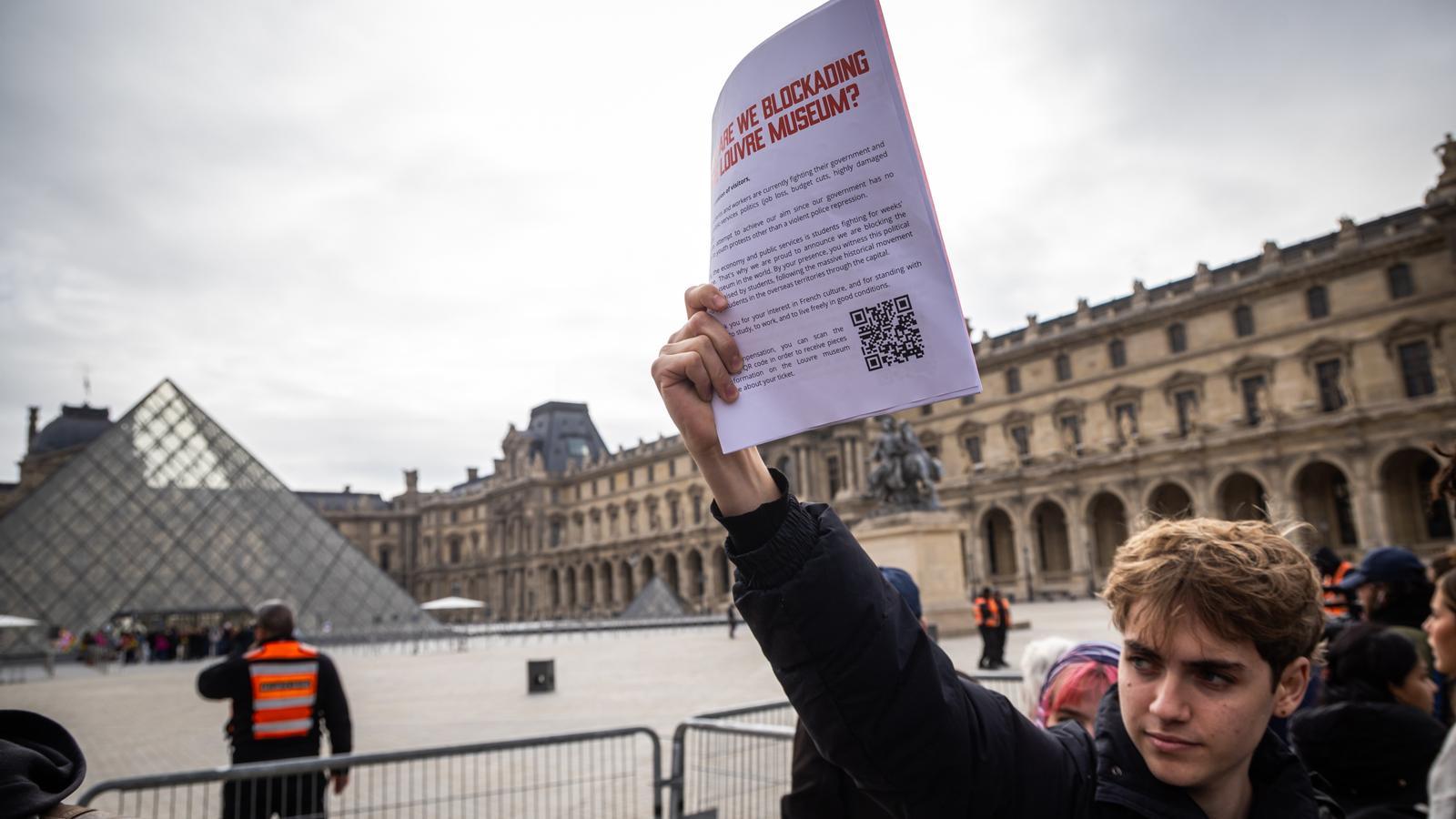 Un manifestante sostiene un cartel donde se lee "¿Por qué bloqueamos el Museo del Louvre?", mientras impiden la entrada del museo en apoyo a las protestas por la educación y el coste de la vida en Francia, el 19 de octubre de 2026.