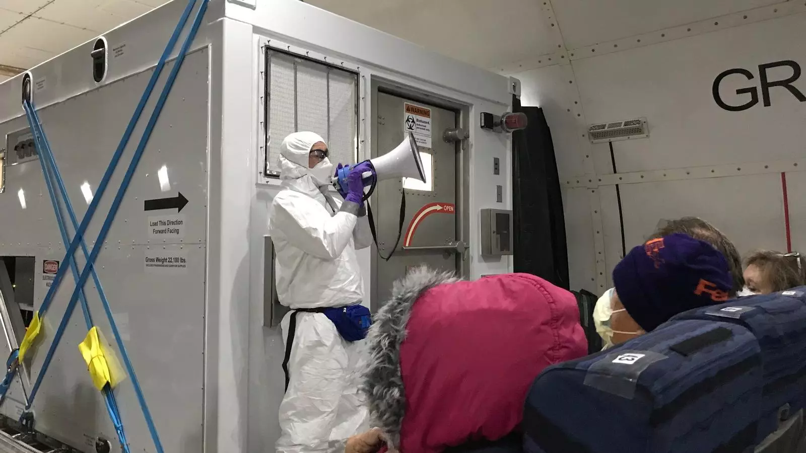 Un funcionari sanitari dels Estats Units davant d’una unitat portàtil de contenció bio parla amb els passatgers nord-americans del creuers Diamond Princess, al ser traslladats en un avió d’evacuació noliejat per volar cap als Estats Units