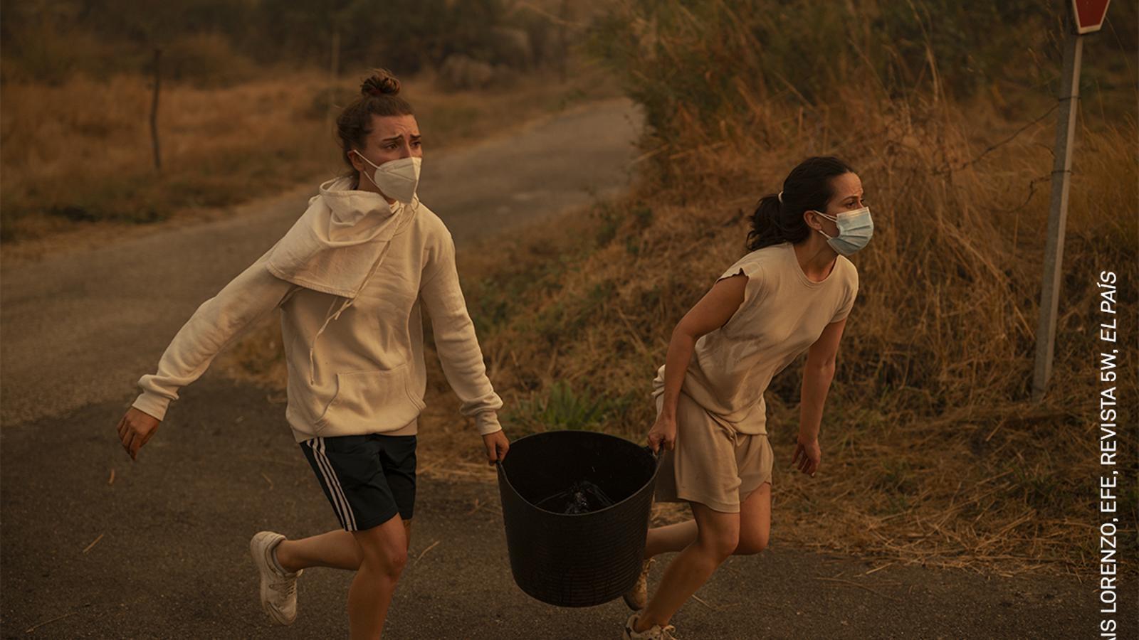 Two women run with a bucket of water to help put out a forest fire in Carballeda de Avia. Orense, Galicia, Spain, August 17, 2025.
