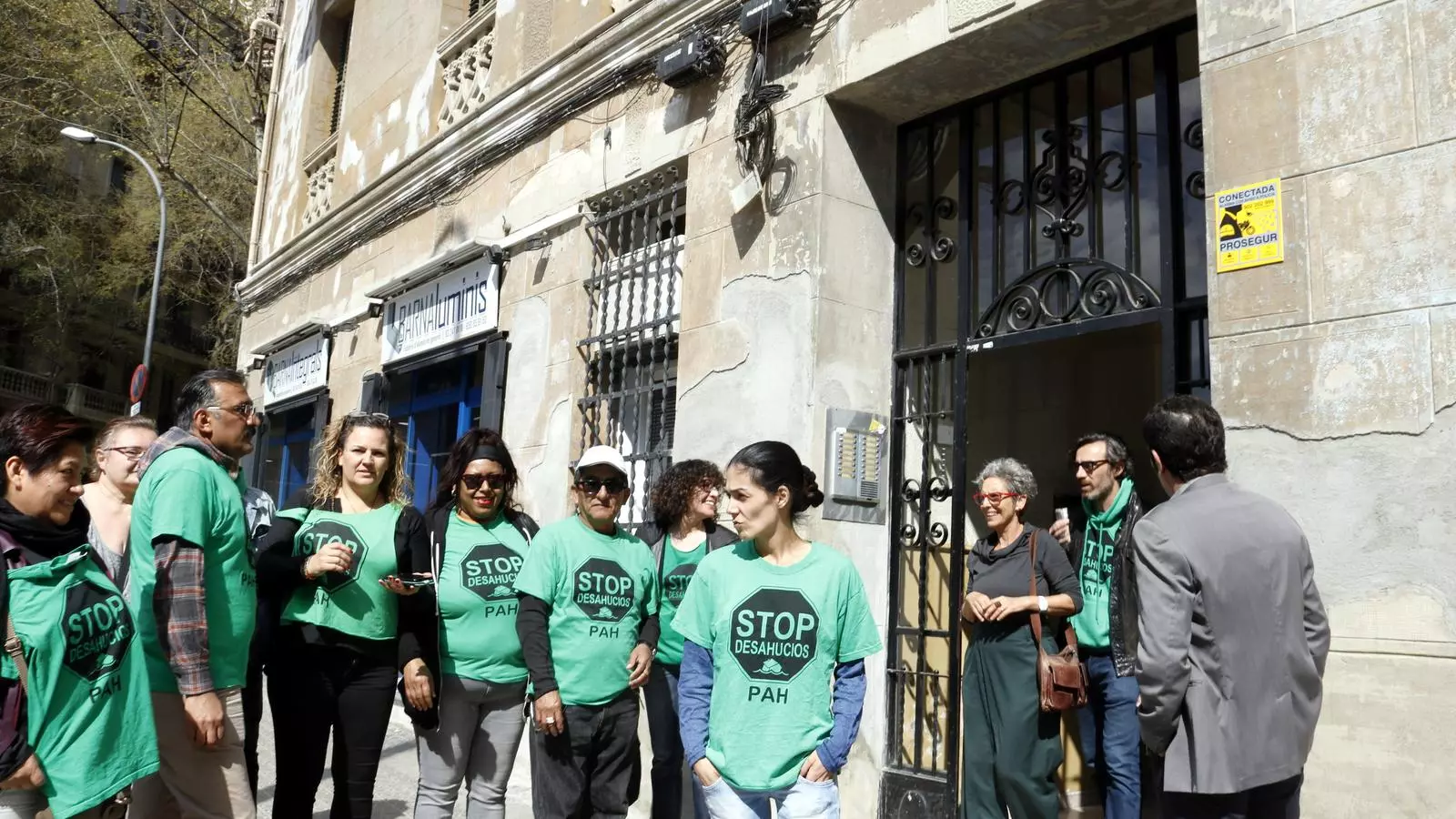 Membres de la PAH Barcelona, veïns de l'edifici i la urbanista i experta en dret a l'habitatge Raquel Rolnik (sortint per la porta), davant el bloc Aragó 477