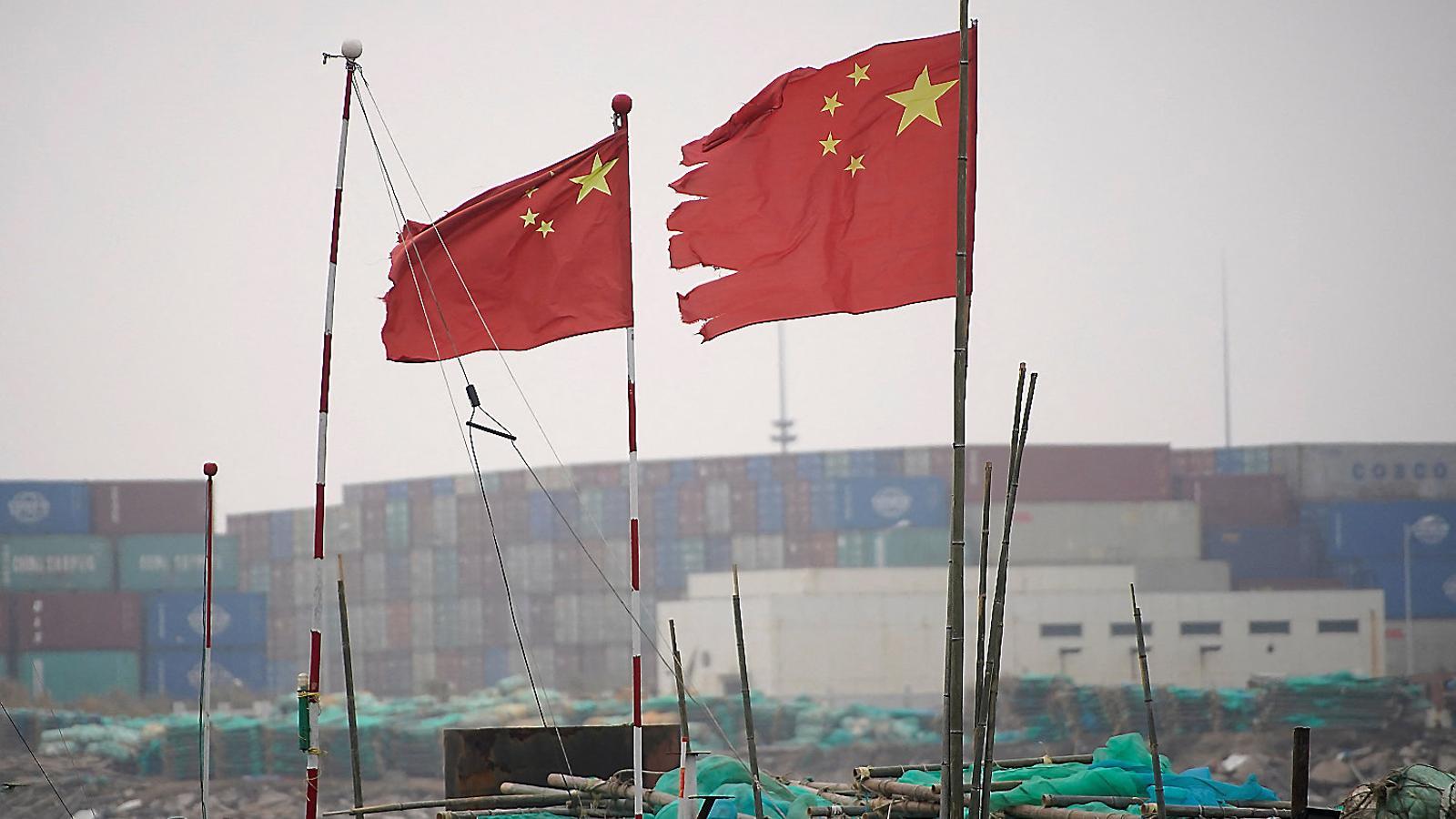 Two flags of China waving in front of containers at the port of Shanghai, in the east of the country.