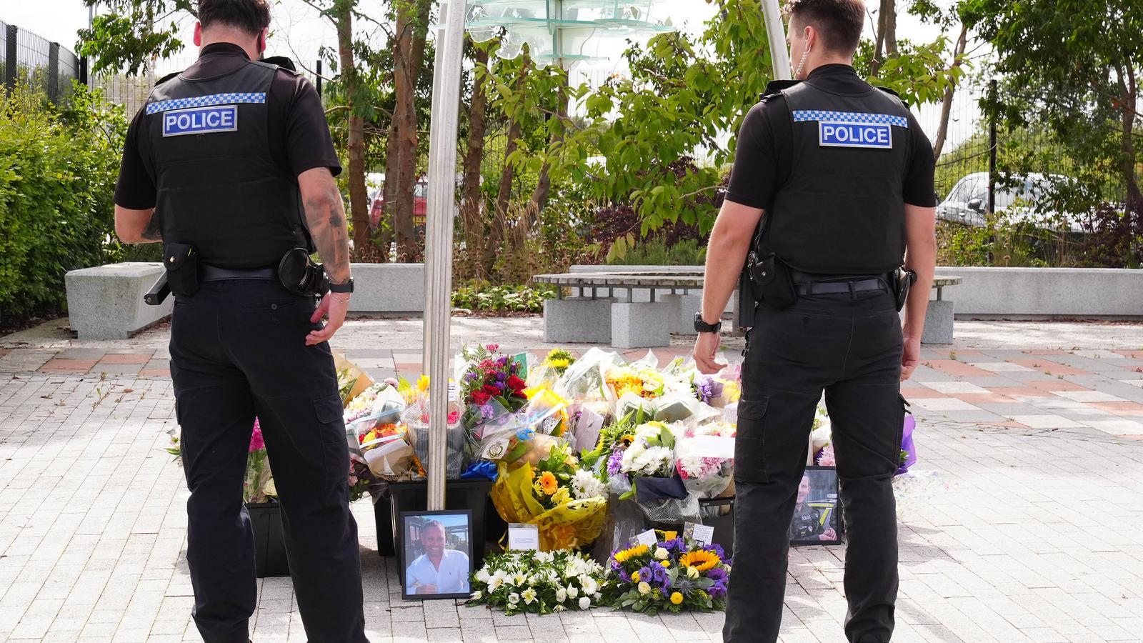A couple of police officers observe the flowers laid in front of the Cleveland police headquarters, in Middlesbrough, after the death in the line of duty of officers Matthew Blades and Tom Clough, in the early hours of Saturday.