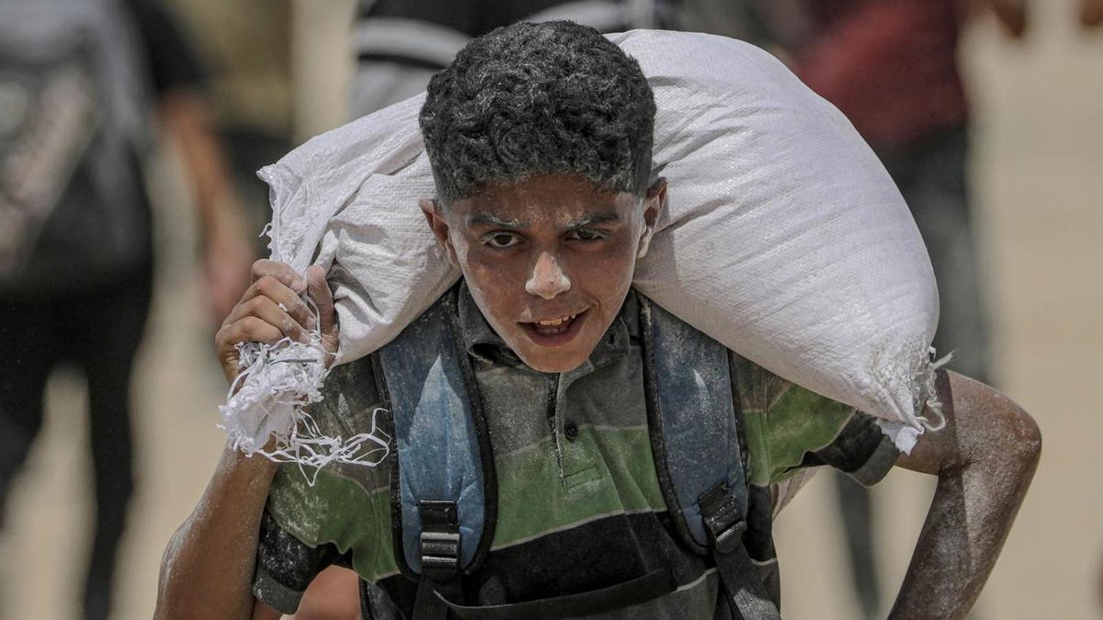 A young Palestinian man carries a sack of flour at the Zikim food distribution point in the northern Gaza Strip on August 8.