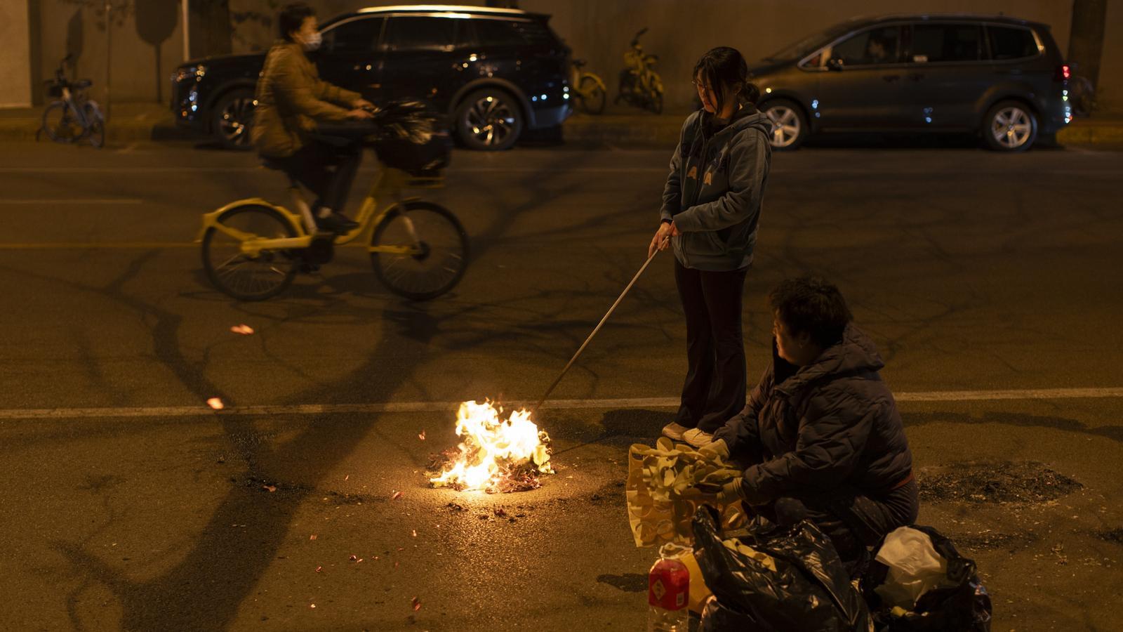 Una mujer quema billetes en la calle como ofrendas a sus familiares difuntos durante el Festival Qingming en Pekín.