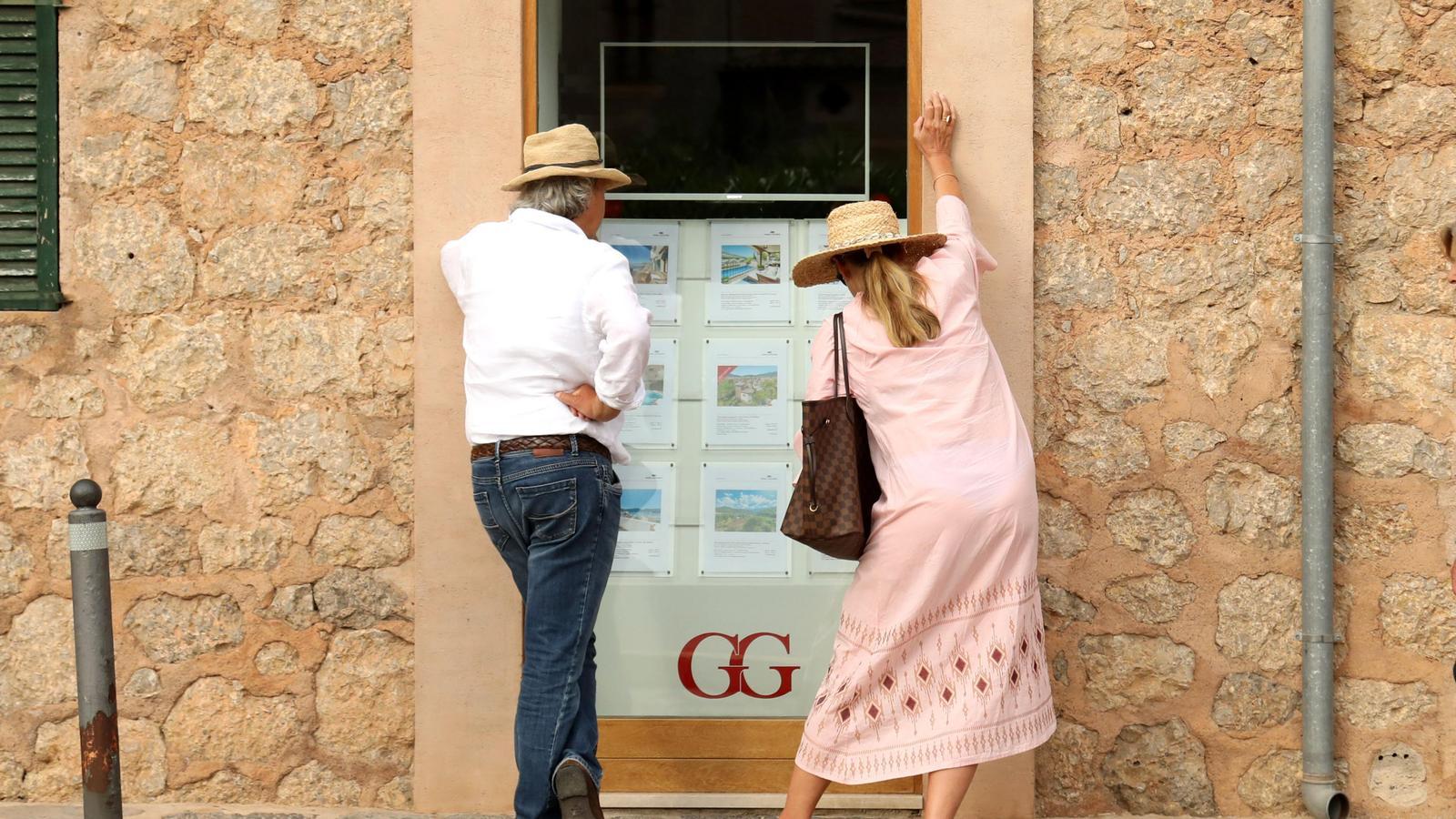Turistes mirando una inmobiliaria en Deià.