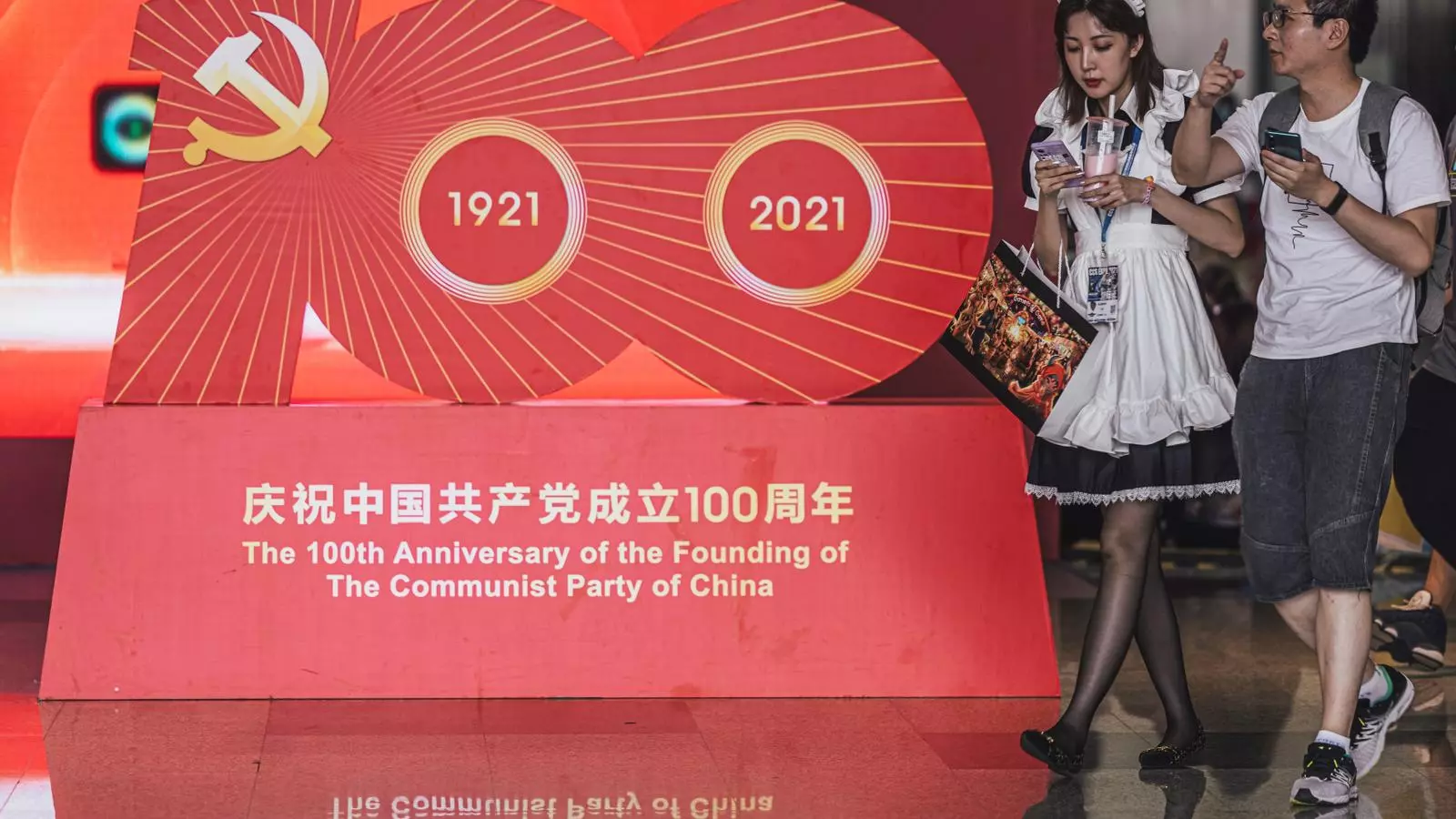 Dos visitantes andan ante un estand conmemorativo del centenario de la fundación del Partido Comunista de la China