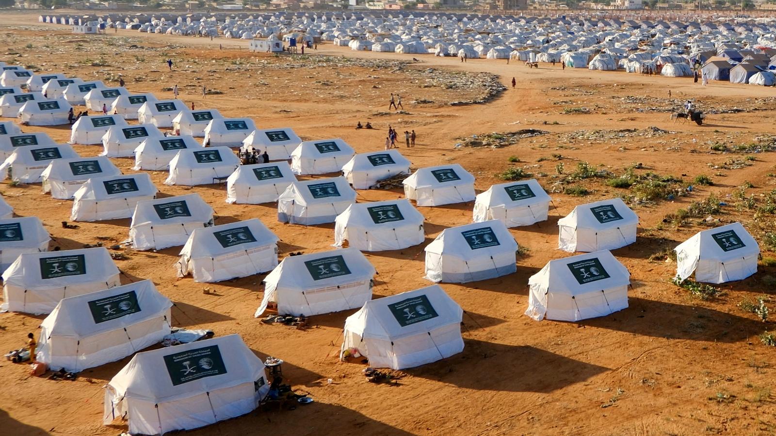 Algunas personas caminan entre tiendas de campaña con el logotipo de Arabia Saudí, en un campo de refugiados en El-Obeid, en Sudán.
