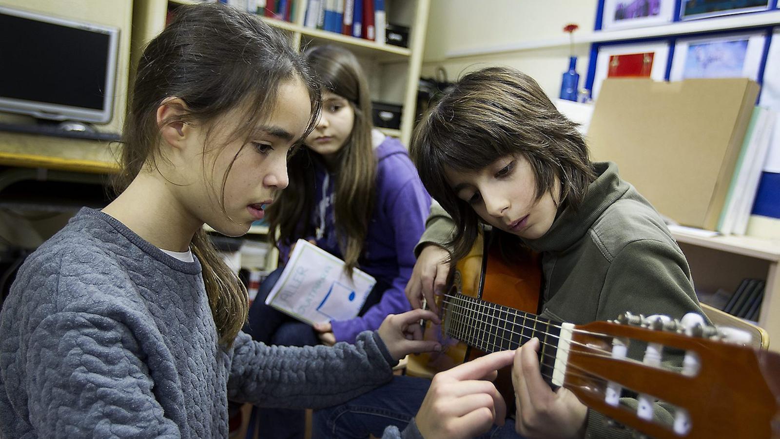 L’ALUMNE FA DE PROFE 
 Una alumna de l’Escola Sant Felip Neri ensenyant a tocar la guitarra a un altre.