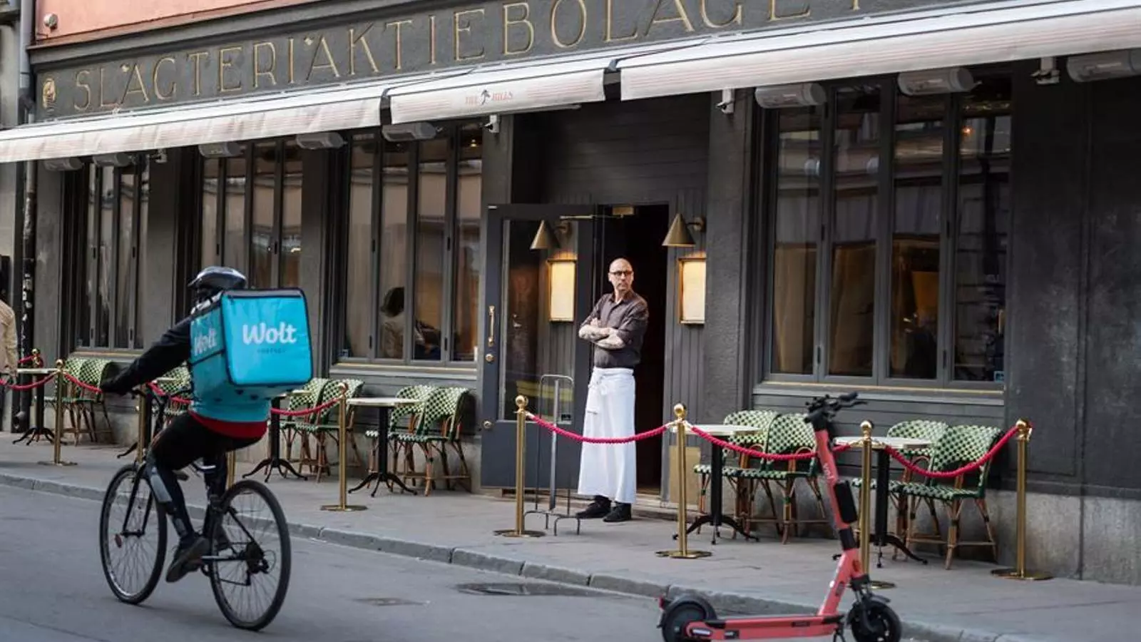Un cambrer esperant clients a la porta del restaurant, mentre passa en bicicleta un 'ridder' per un carrer d'Estocolm