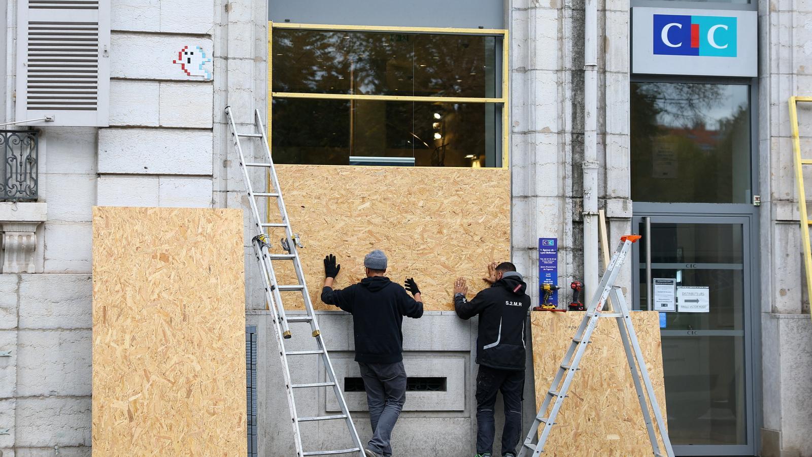 Trabajadores instalan paneles de madera para proteger los escaparates de una sucursal del banco CIC en Lyon, antes de las protestas convocadas para este sábado.
