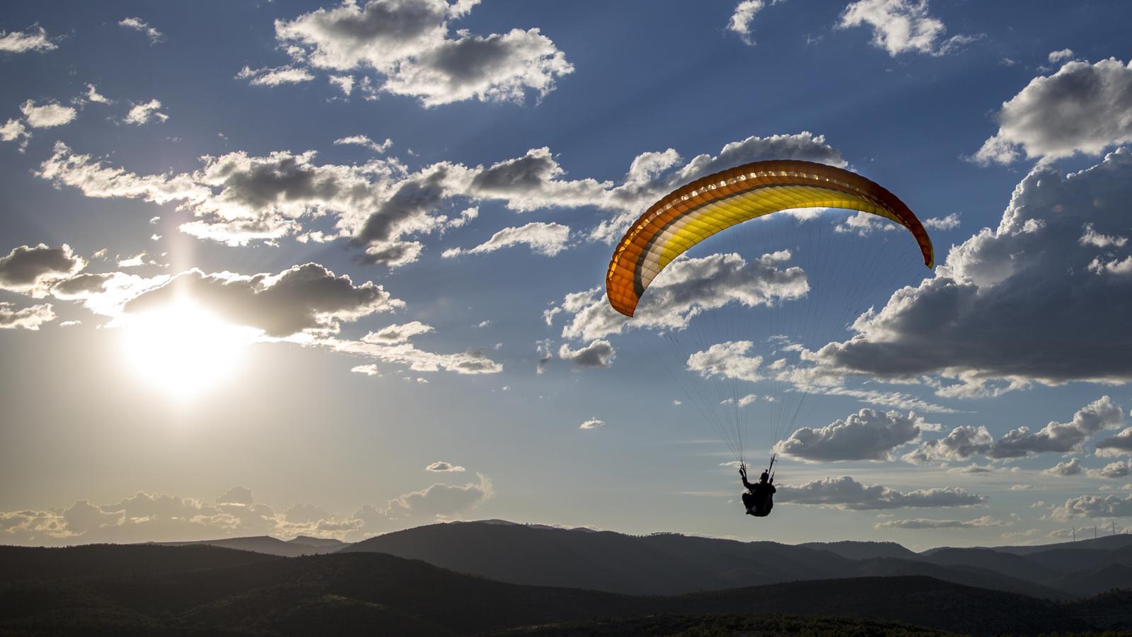 A paraglider takes off from a hill in a stock image.