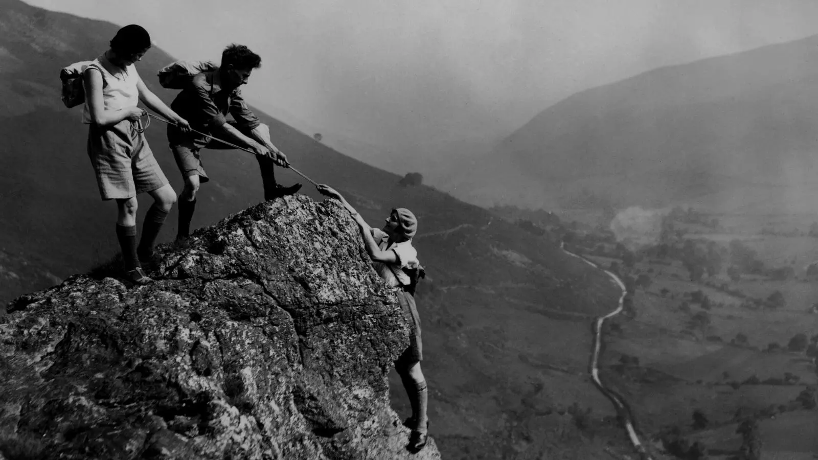 Excursionistes ayudándose a llegar a la cumbre de una montaña.