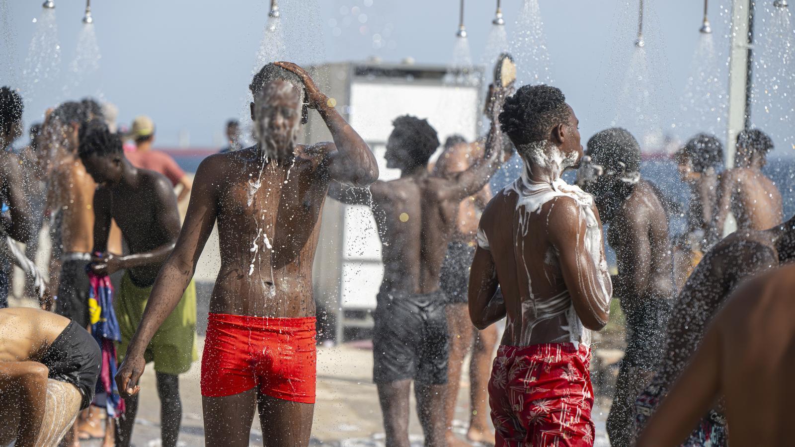 Jóvenes duchándose en unos baños de la playa del Trampolín de Ceuta.