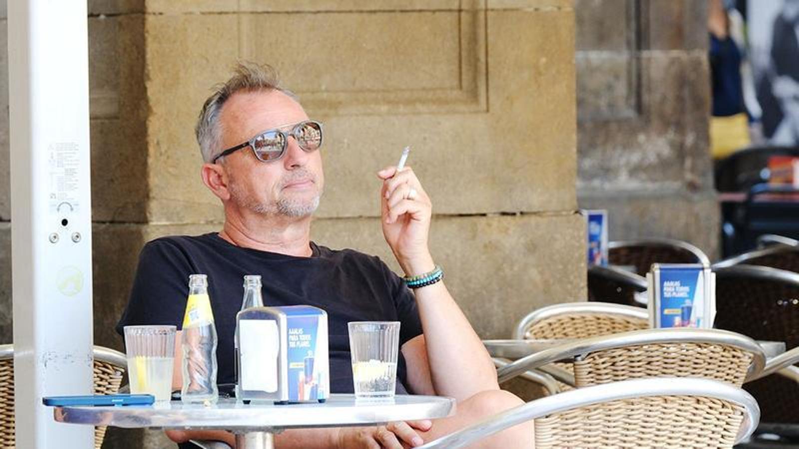 Un hombre fumando en la terraza de un bar.
