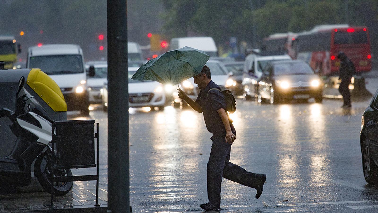 A man with a half-broken umbrella crosses a zebra crossing in Barcelona