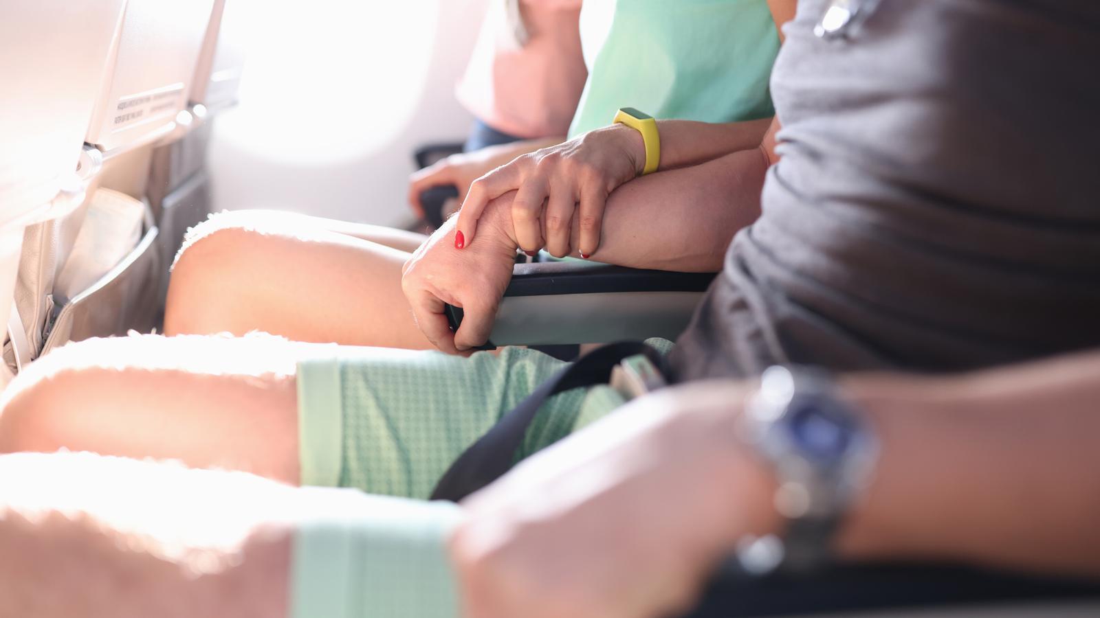 A woman tightly grips a man's hand during a flight. A scene that reflects the fear of flying.