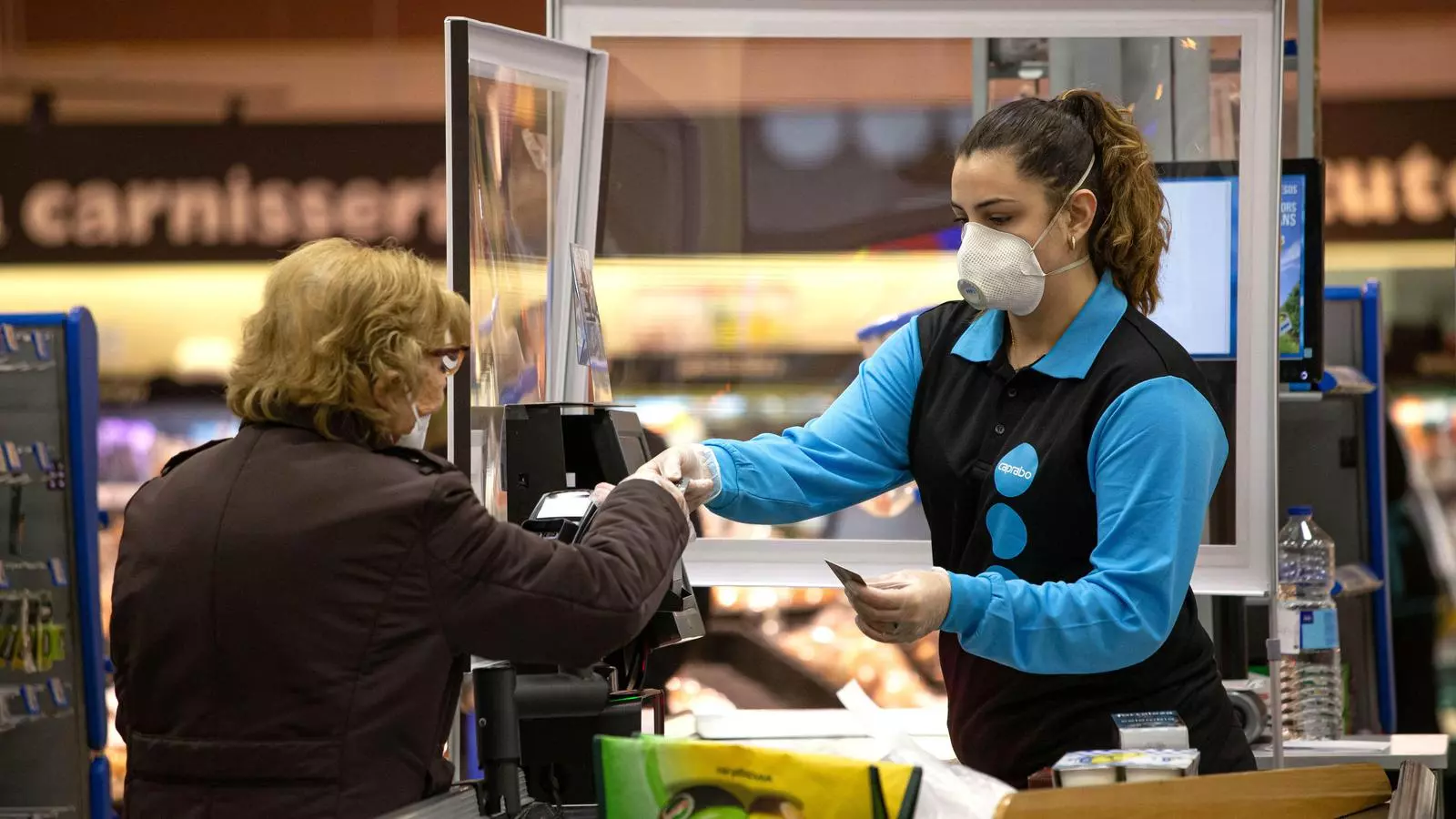 Una senyora paga la compra a una caixera al supermercat durant la pandèmia del covid-19