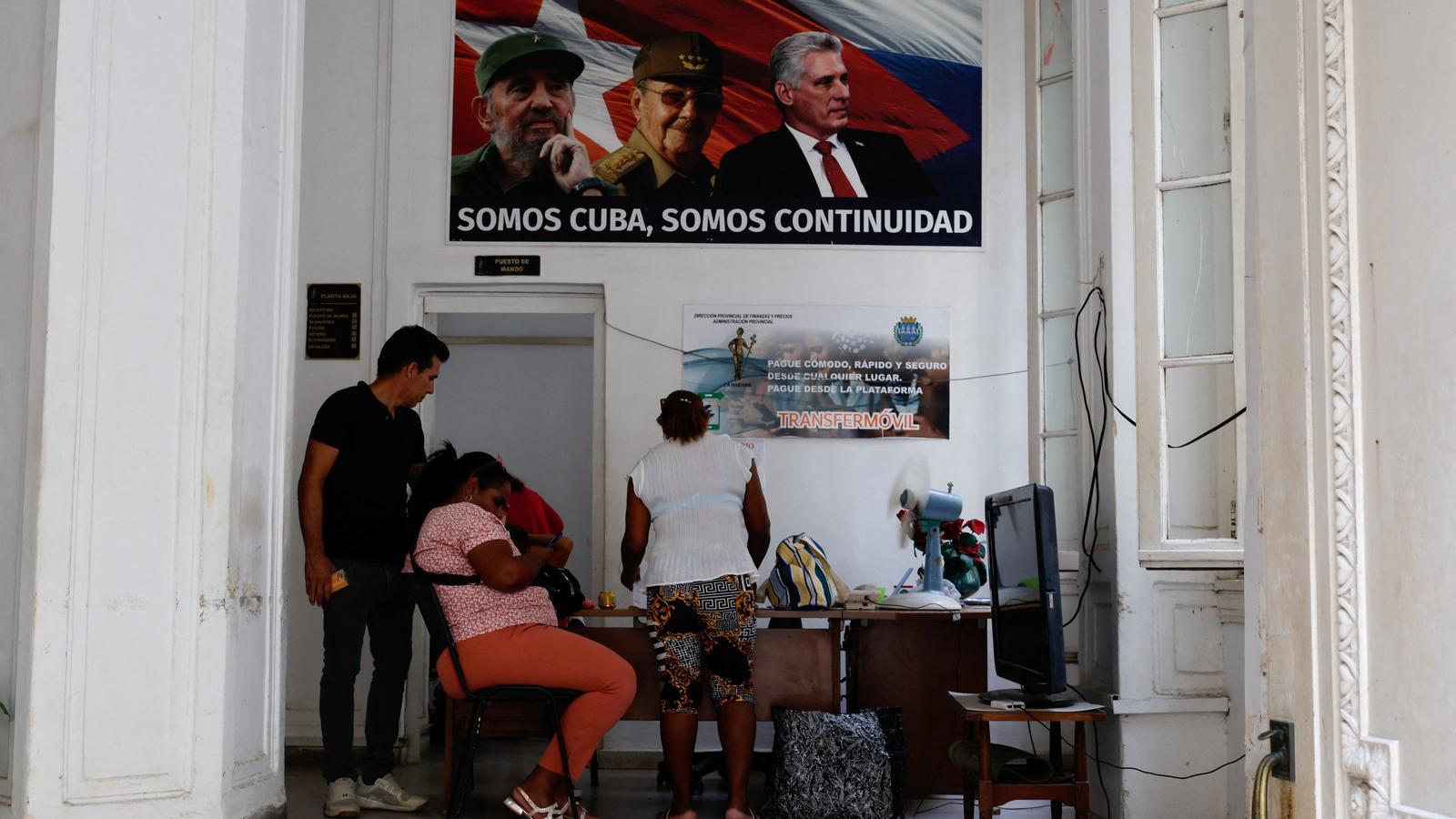 Trabajadores en una oficina del Ministerio de Finanzas y Precios bajo un póster en el que aparecen Fidel y Raúl Castro y el actual presidente, Miguel Díaz-Canel.