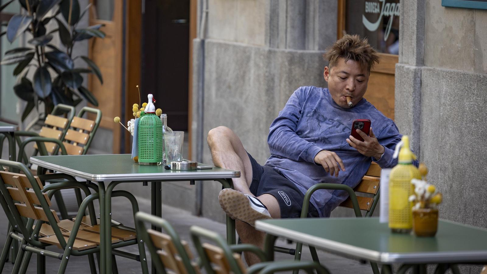 Un señor se fuma un cigarro en la terraza de un bar del Raval, hoy por la tarde