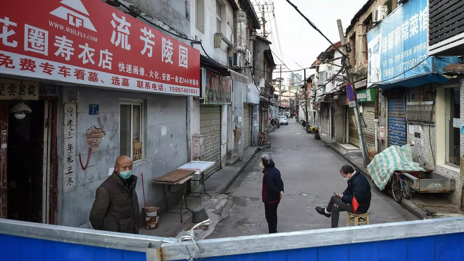 Persones davant d'una barrera per evitar l'entrada de gent a un barri de Wuhan, Xina