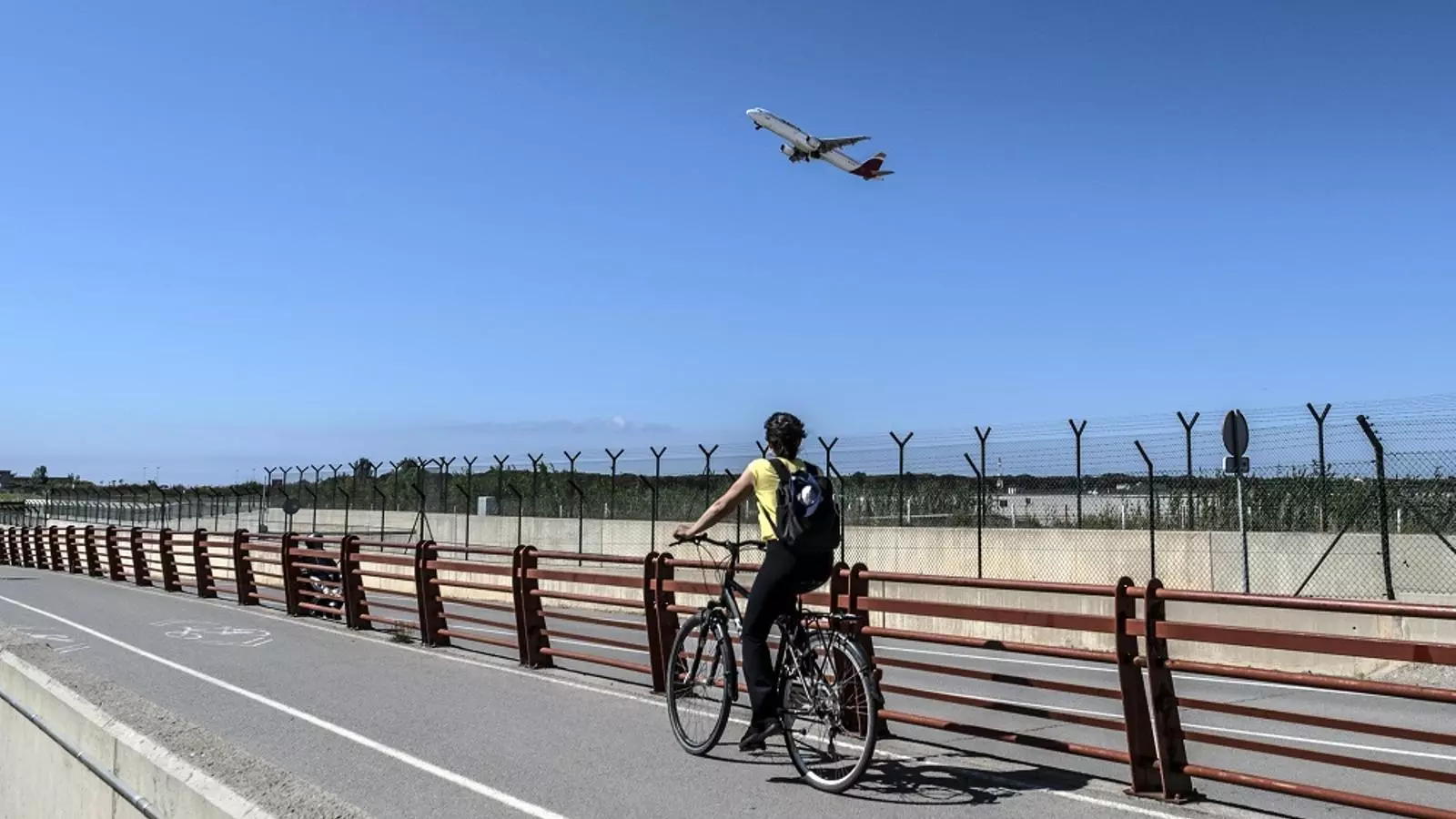 Un ciclista observa un avió enlairar-se als voltants de l'Aeroport del Prat