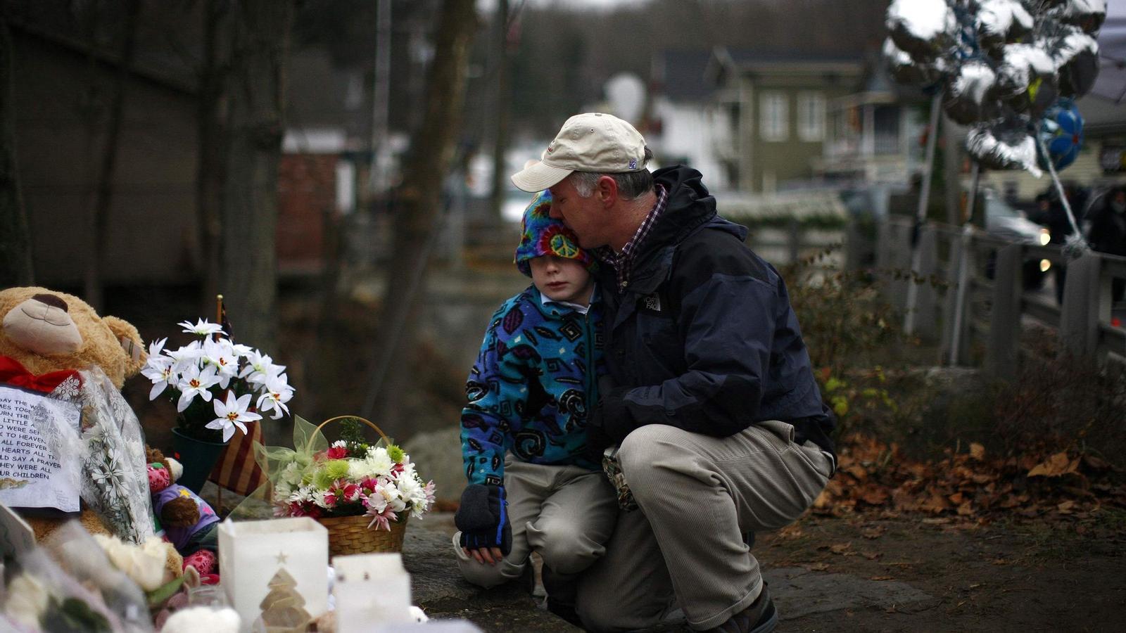 Un home abraça un nen en un petit homenatge a prop de l'escola de Newtown.