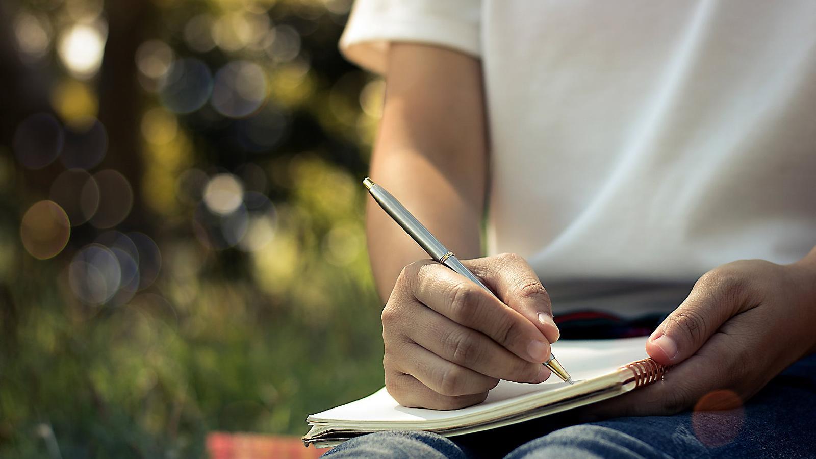 A person writing in a notebook in a park.