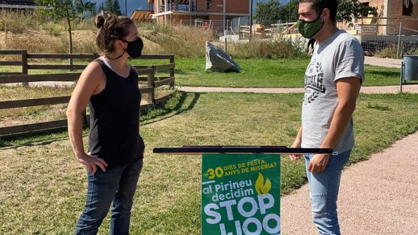 Dos portaveus de la Plataforma Stop JJOO, Helena Guillén i Bernat Lavaquiol, presentant l'entitat davant d'un bloc d'habitatges en construcció a Bellver de Cerdanya. Imatge del 30 d'agost de 2021.